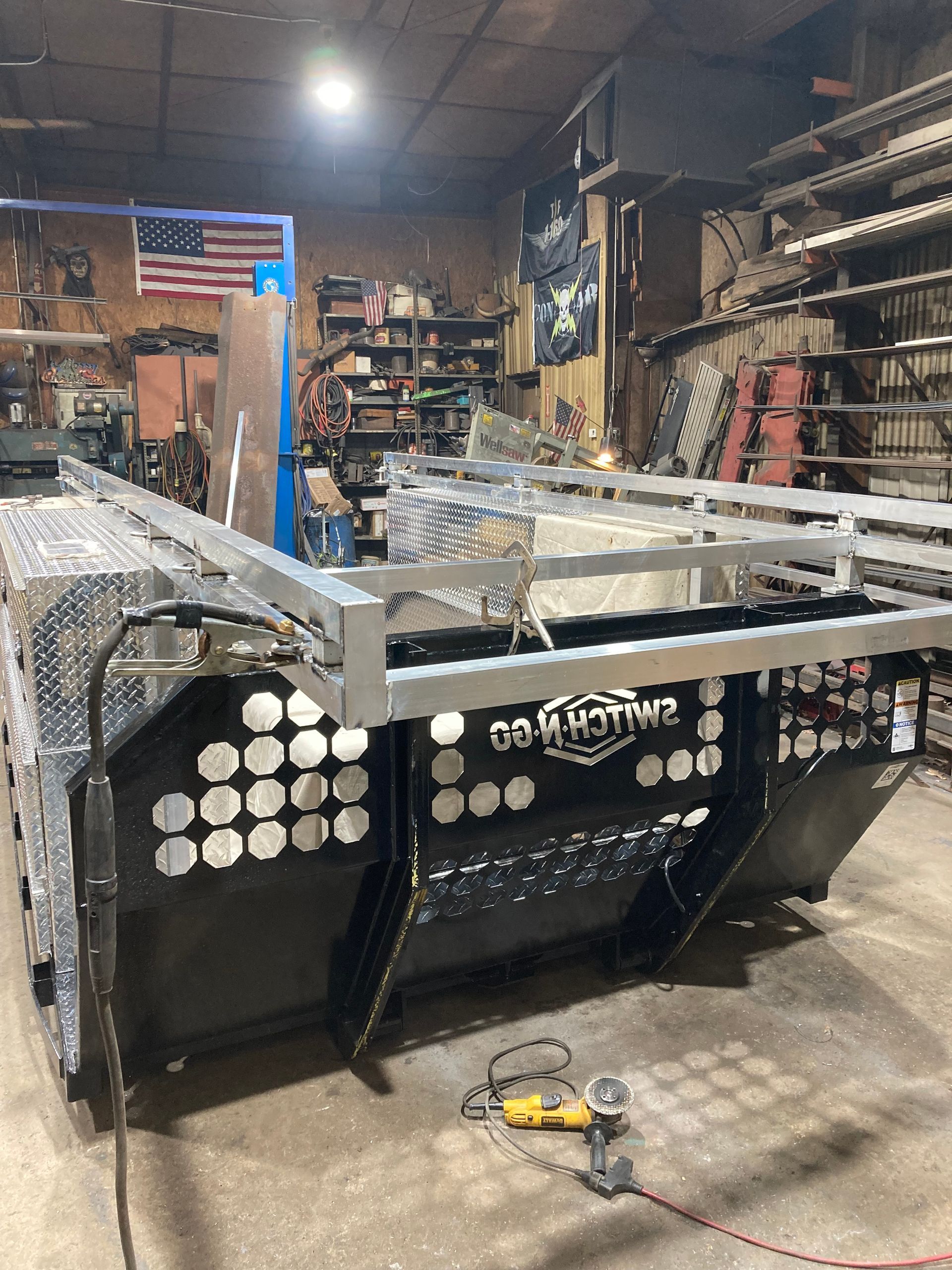 A large black and metallic equipment assembly under construction in a workshop with an American flag on the back wall.