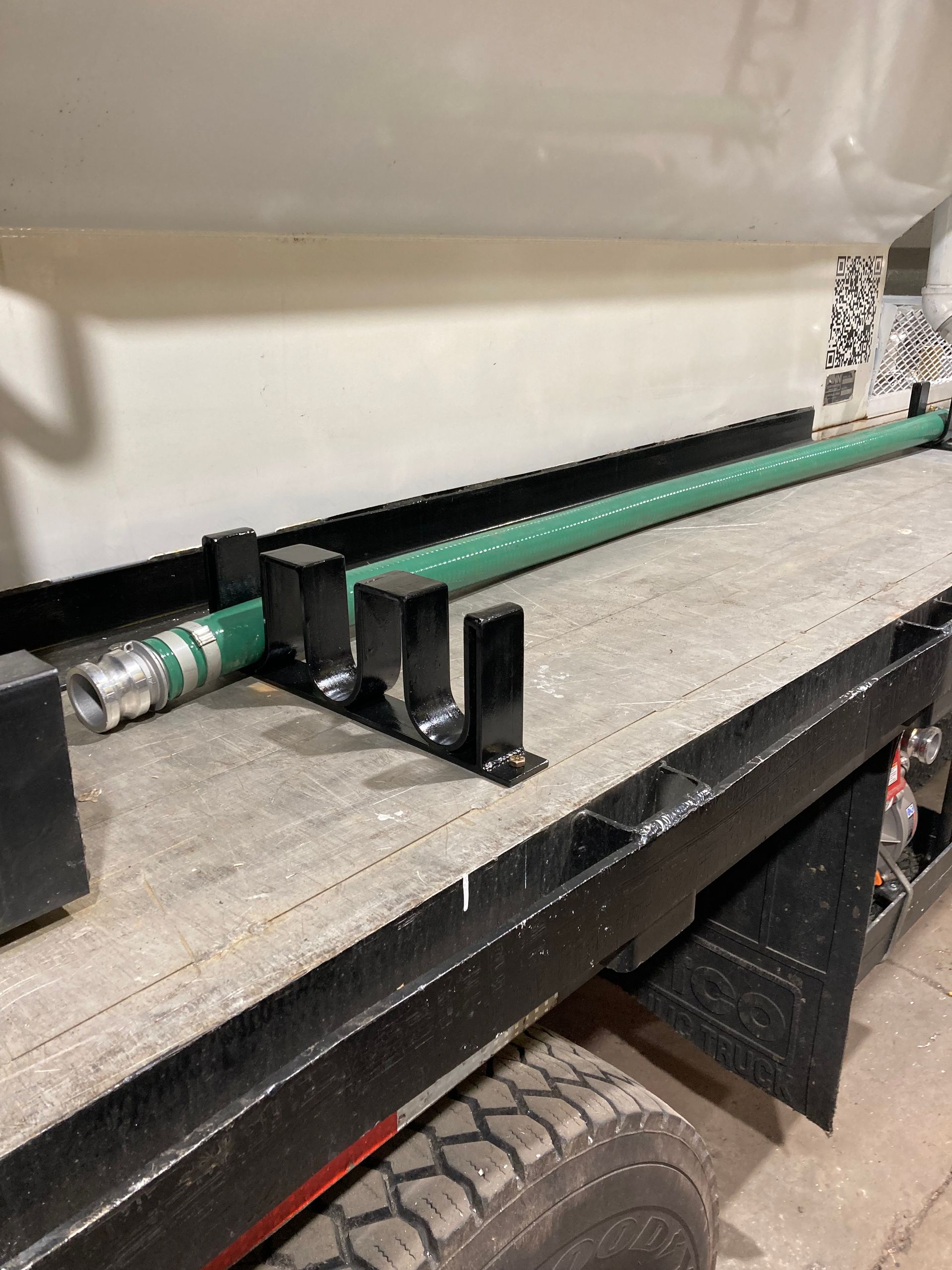 A green suction hose rests in metal cradle mounts on the flatbed of a utility truck.