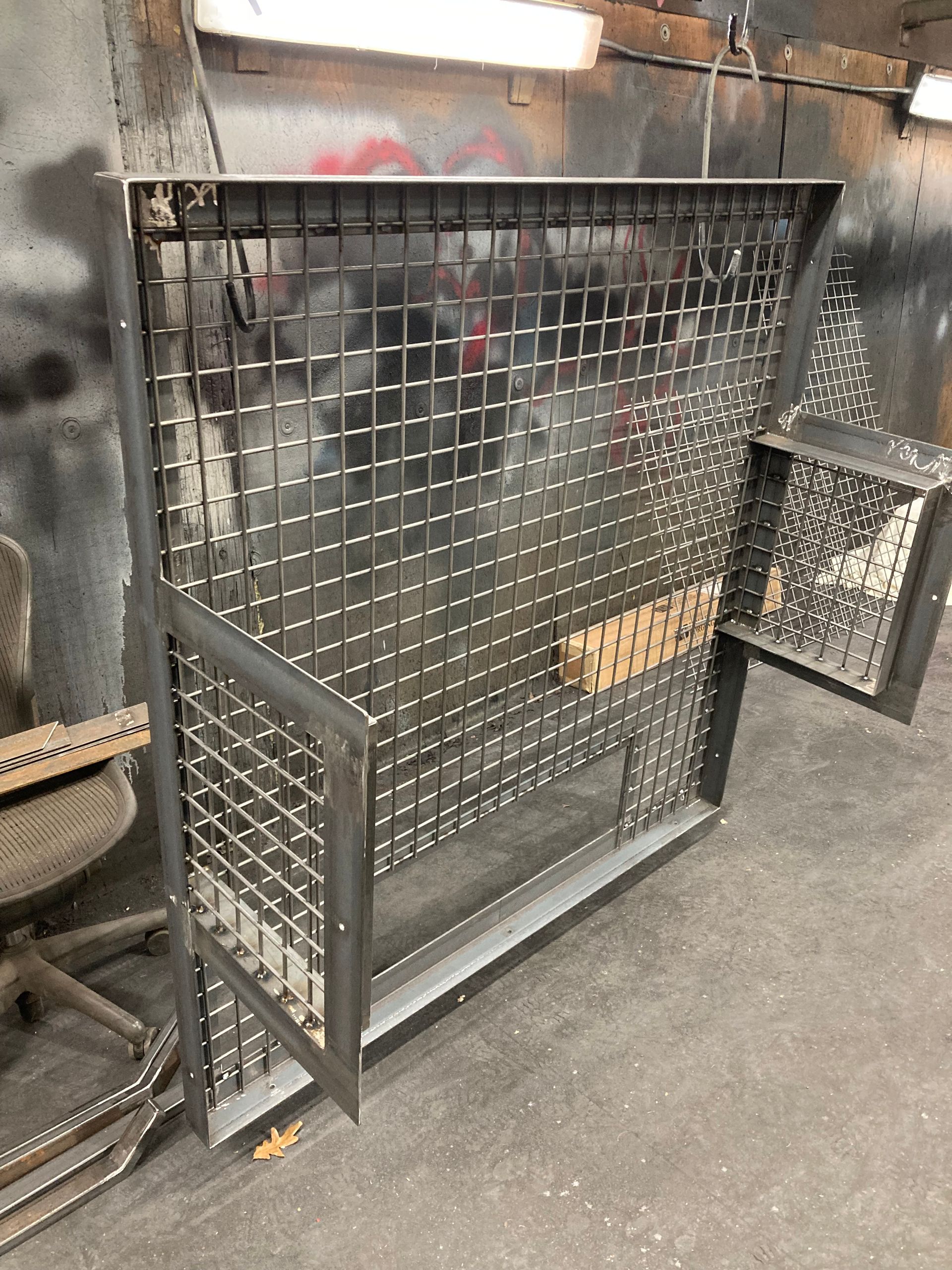 A grey metal wire partition wall with a built-in side shelf, situated in a workshop or industrial space.