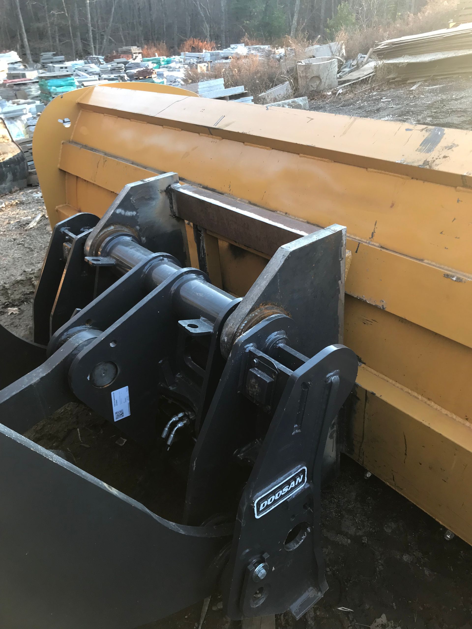 A close-up of a heavy-duty yellow snow plow blade attached to a dark gray steel mounting frame outdoors.
