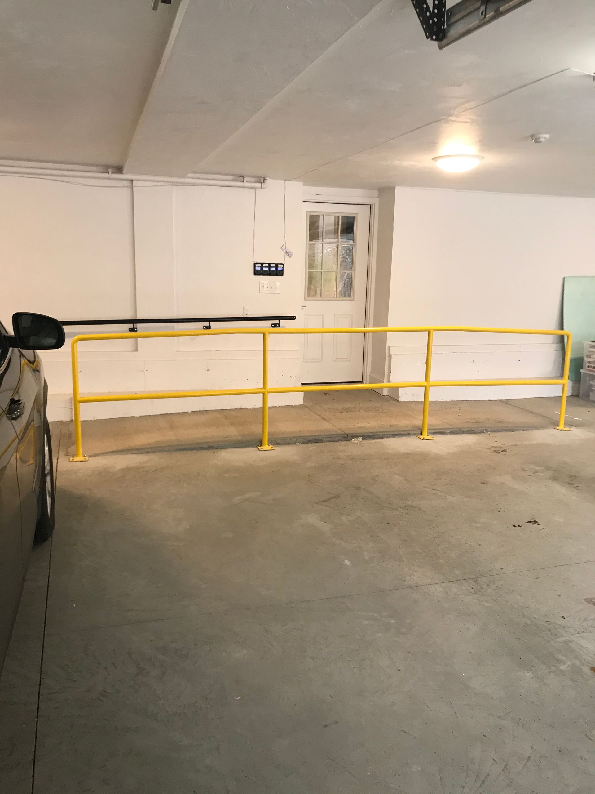 Bright yellow metal safety railing installed in front of a doorway in a concrete garage.