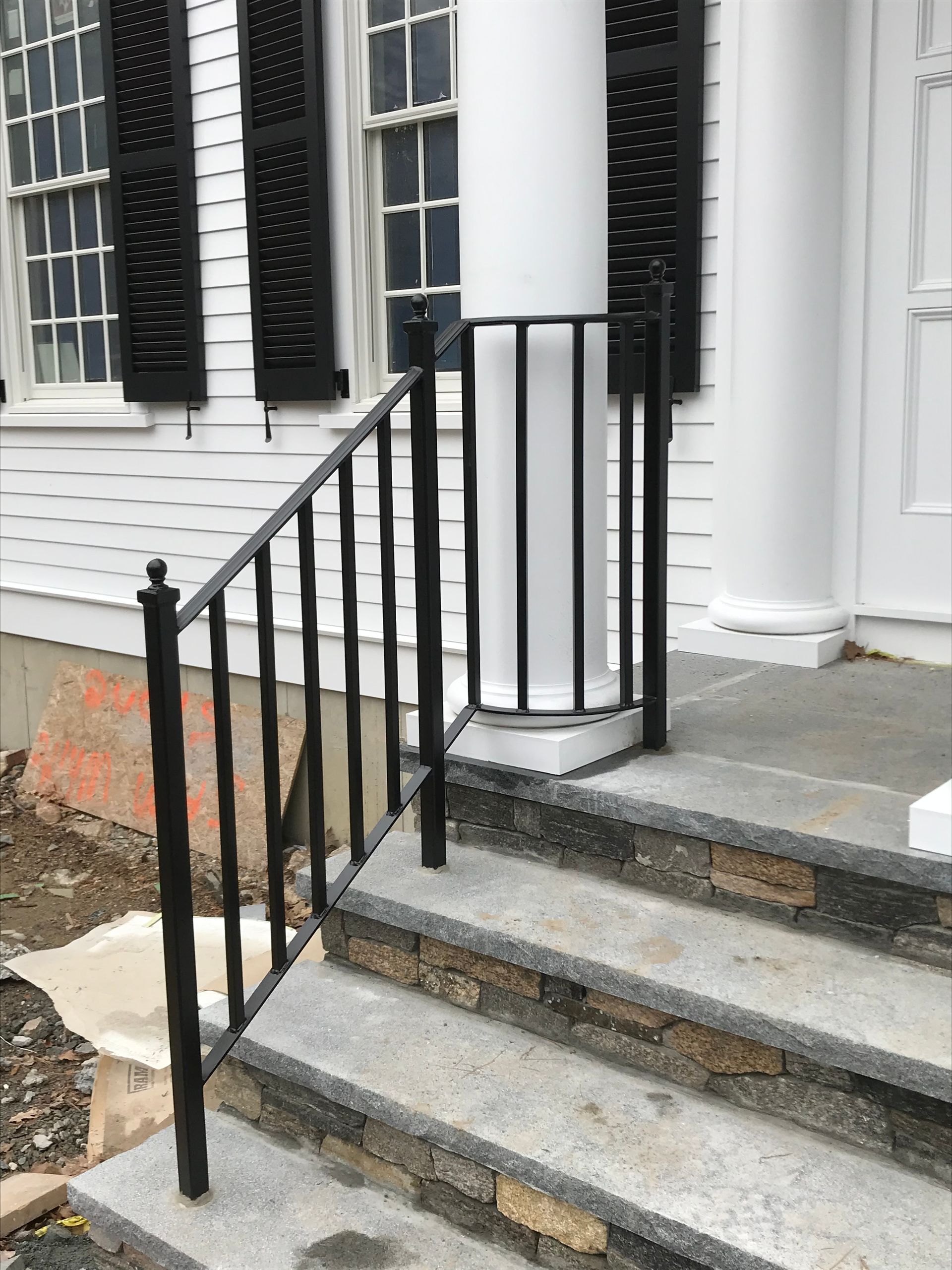 Black metal handrail attached to stone steps leading to a white porch with columns.