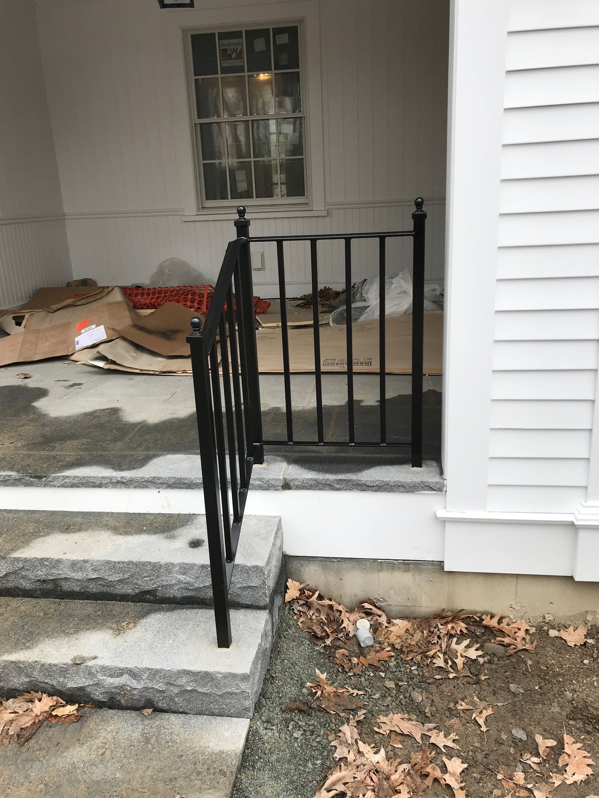 Black metal railing on a front porch with stone steps, white siding, and cardboard on the ground.