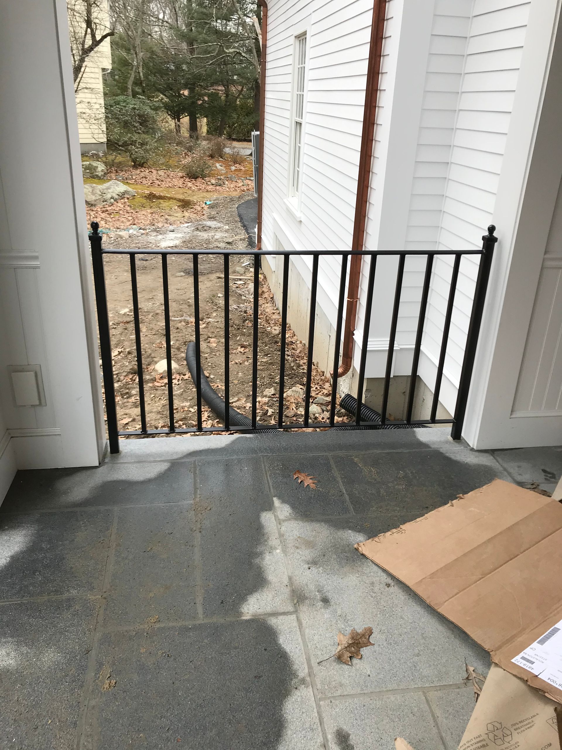 A black metal railing installed on a stone porch, closing off the open space between two white pillars.