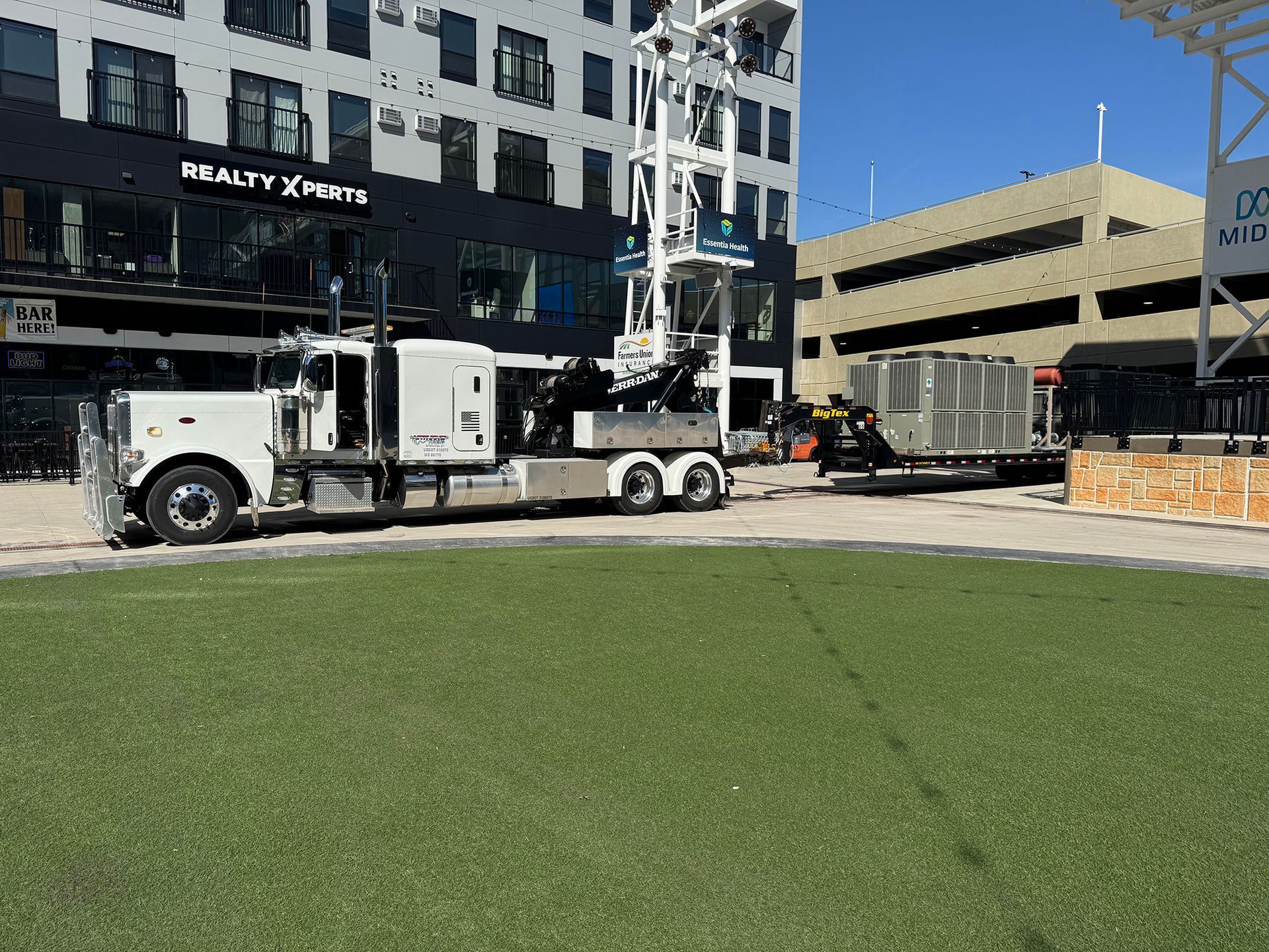 White utility truck with a raised boom parked on a city street beside a building and grassy foreground.