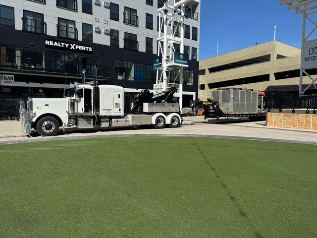 White utility truck with boom lift parked beside a modern building in a sunny urban plaza.