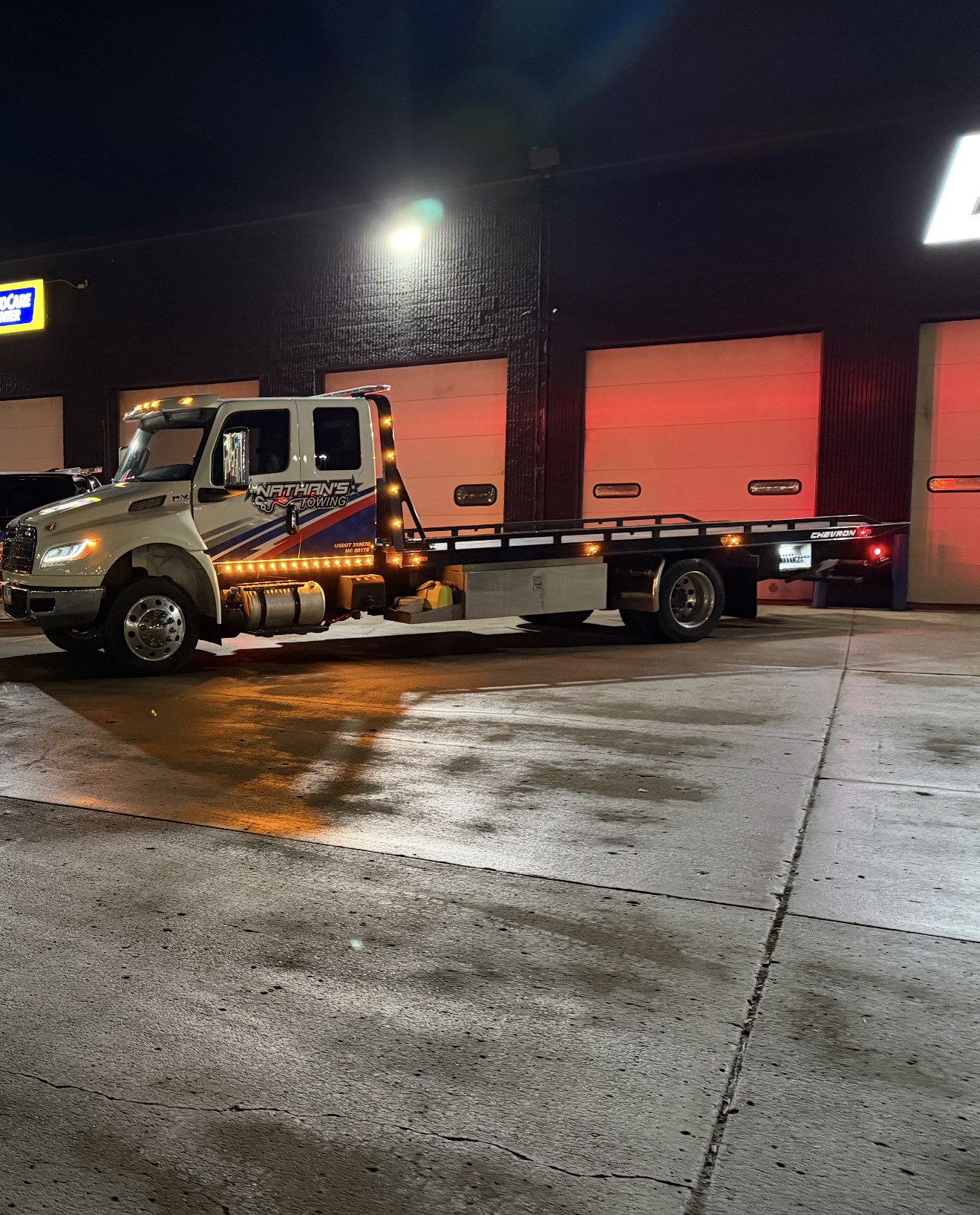 Tow truck parked at a gas station at night beside red-lit garage doors