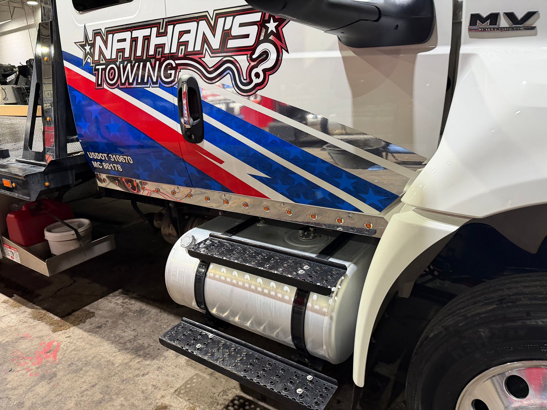 Side view of a white truck with Nathan’s Towing decals, red and blue stripes, and a chrome fuel tank under the cab