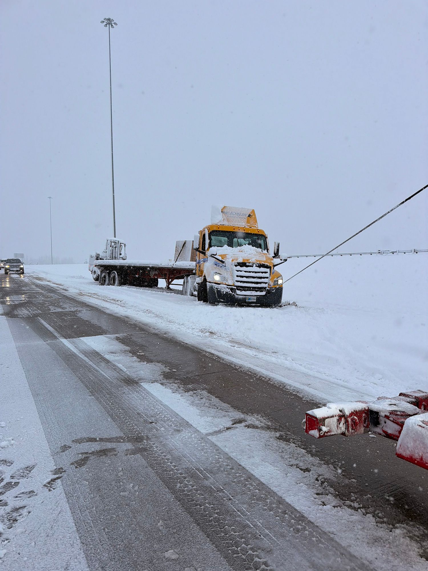 Snowy roadside with a tow truck and flatbed on a wet, slushy road under an overcast sky