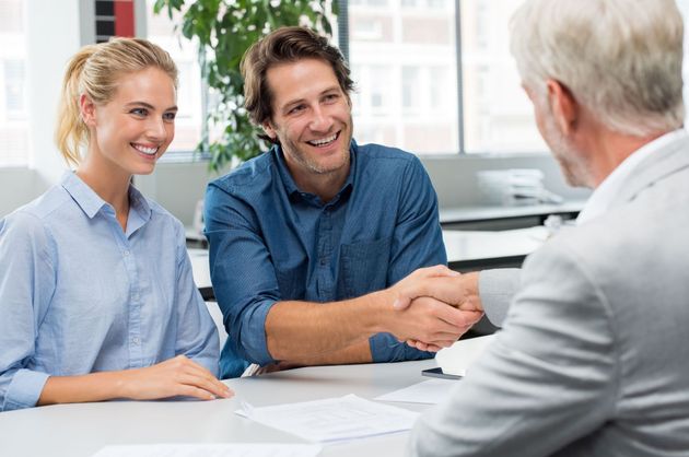 Two people shaking hands with a man across a desk in a bright office.