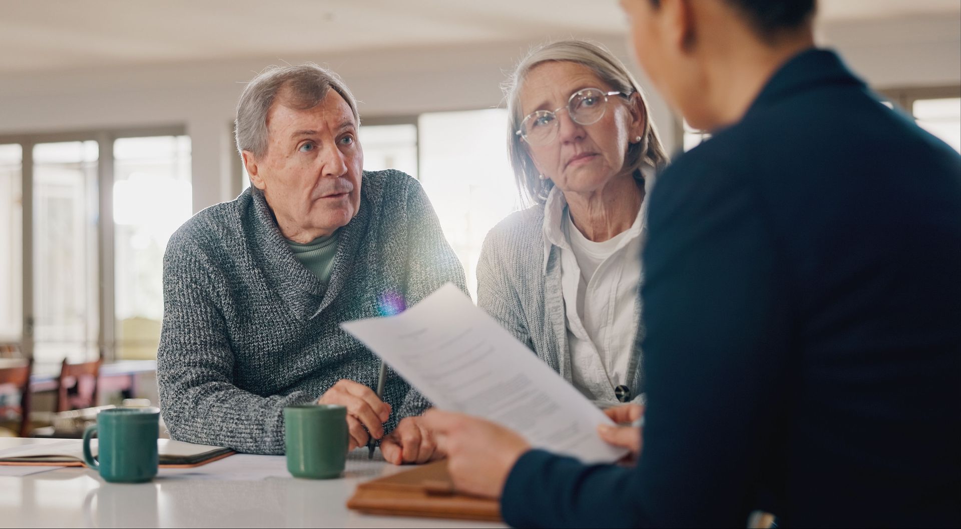 Two people reviewing documents with a consultant at a table in a bright meeting room.