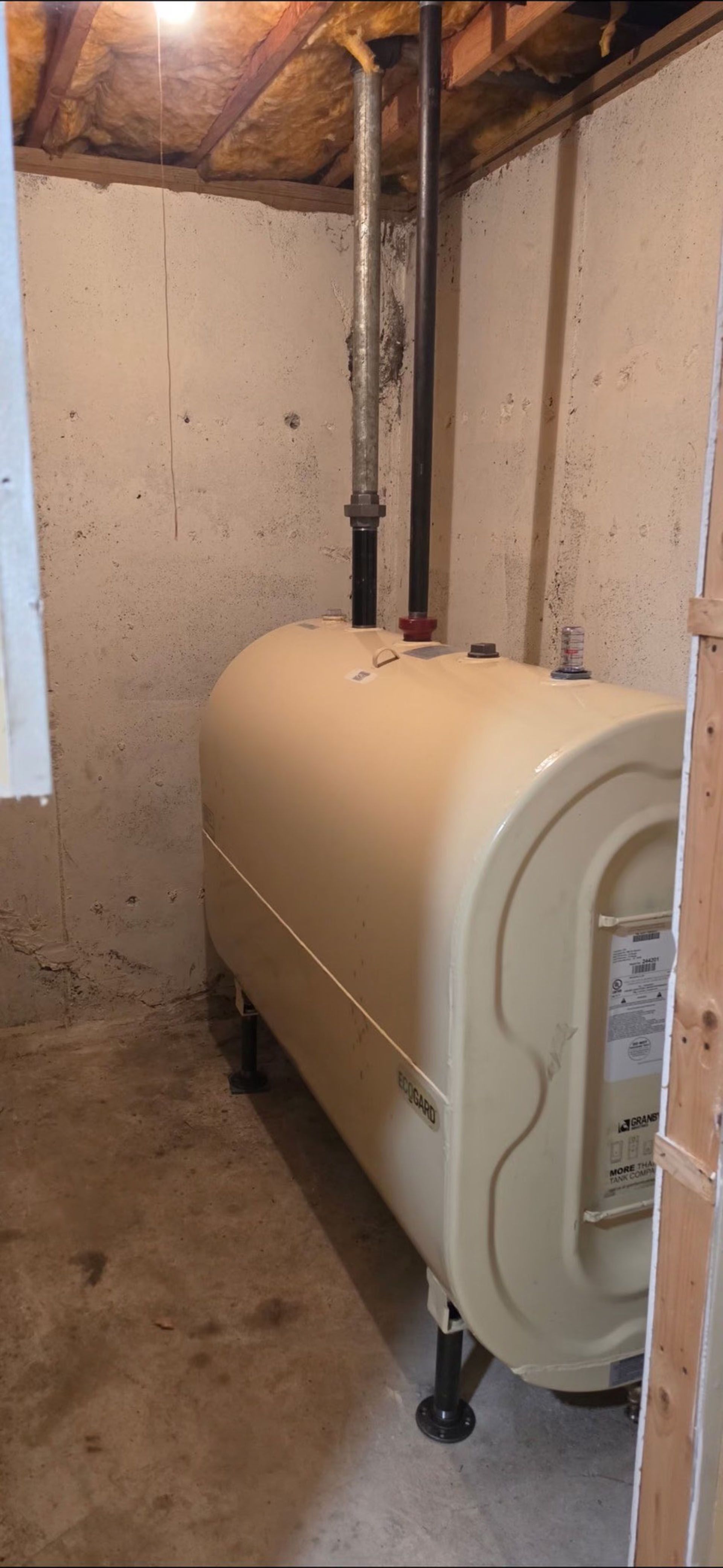 Beige boiler tank in a basement with exposed pipes and unfinished walls