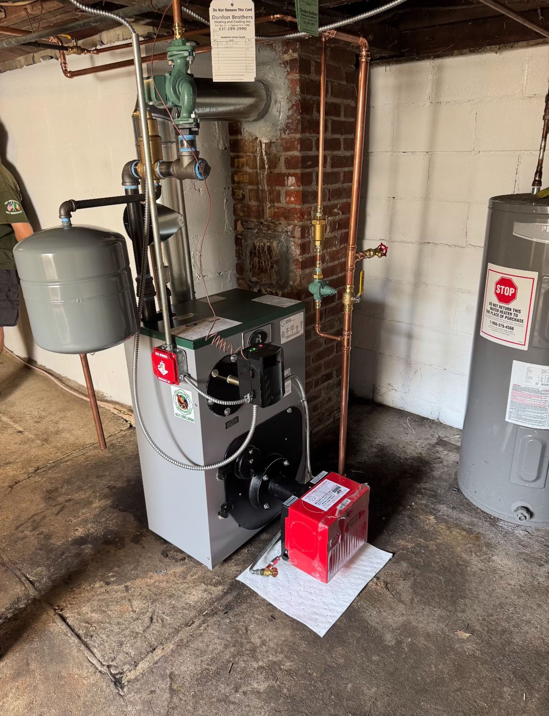 Basement utility area with a furnace, water heaters, and pipes against a brick wall