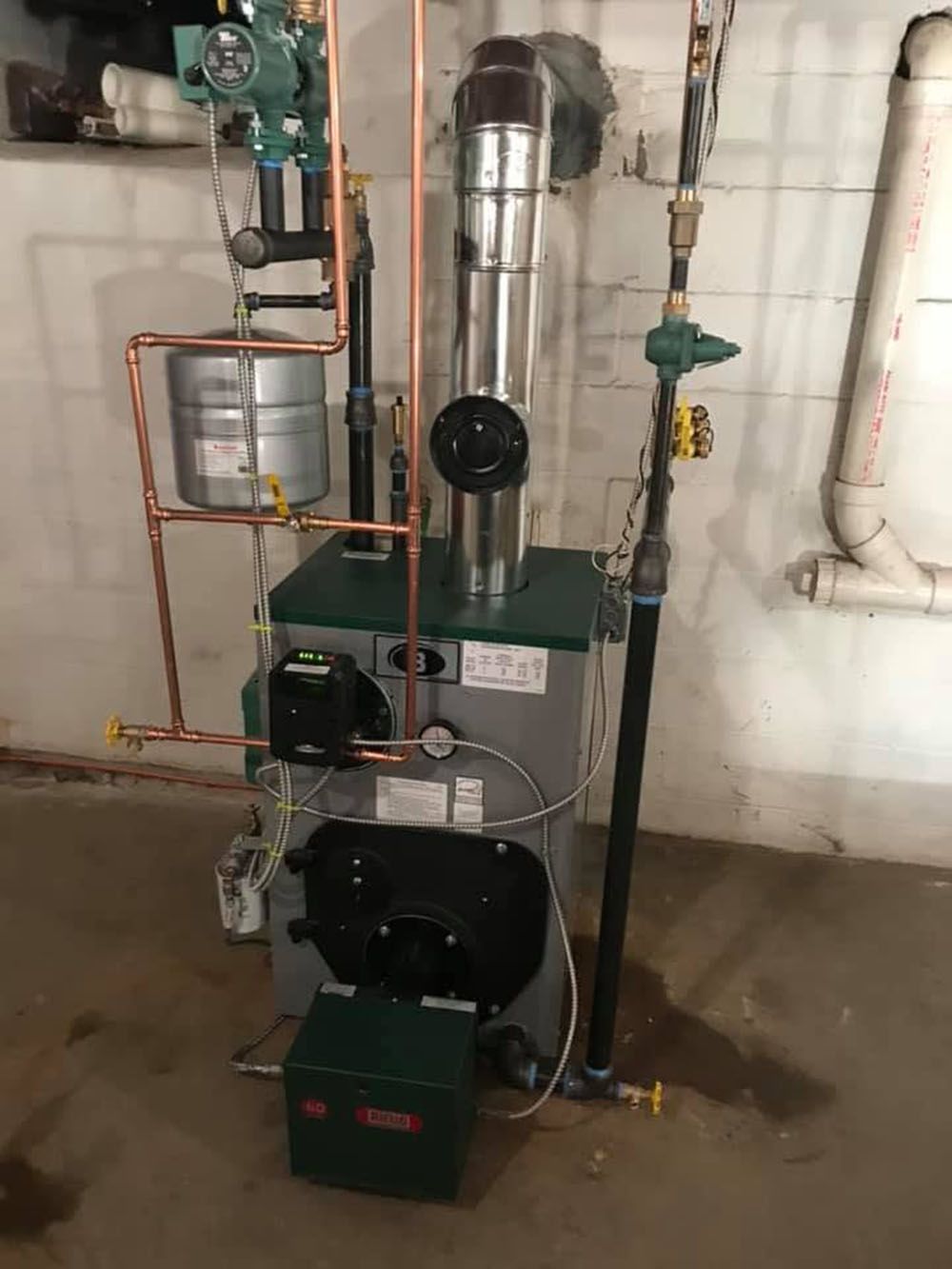 Industrial boiler and piping system in a utility room, with black and silver tanks and copper pipes.