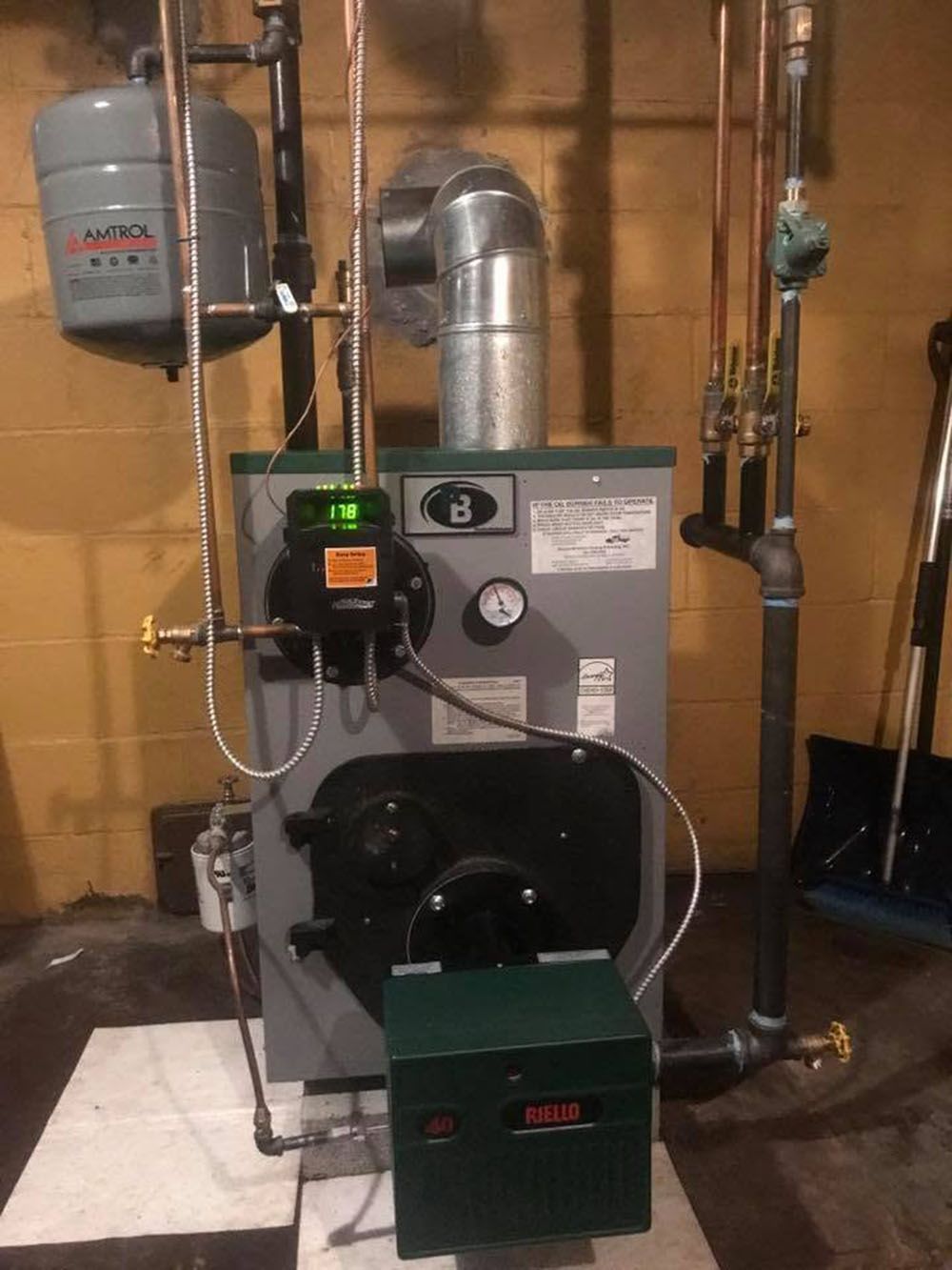 Utility room boiler and HVAC equipment with metal ducting, gauges, and a green furnace unit against unfinished walls