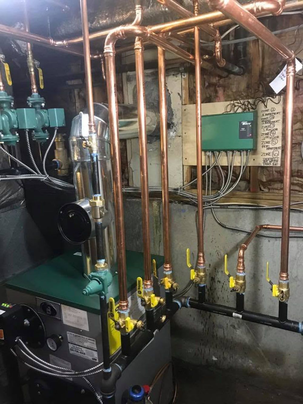 Industrial boiler room with copper pipes, green equipment, gauges, and valves on a concrete floor.