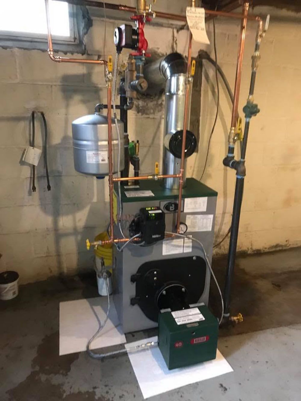 Boiler and plumbing setup in a basement, with pipes, gauges, and a green toolbox in front