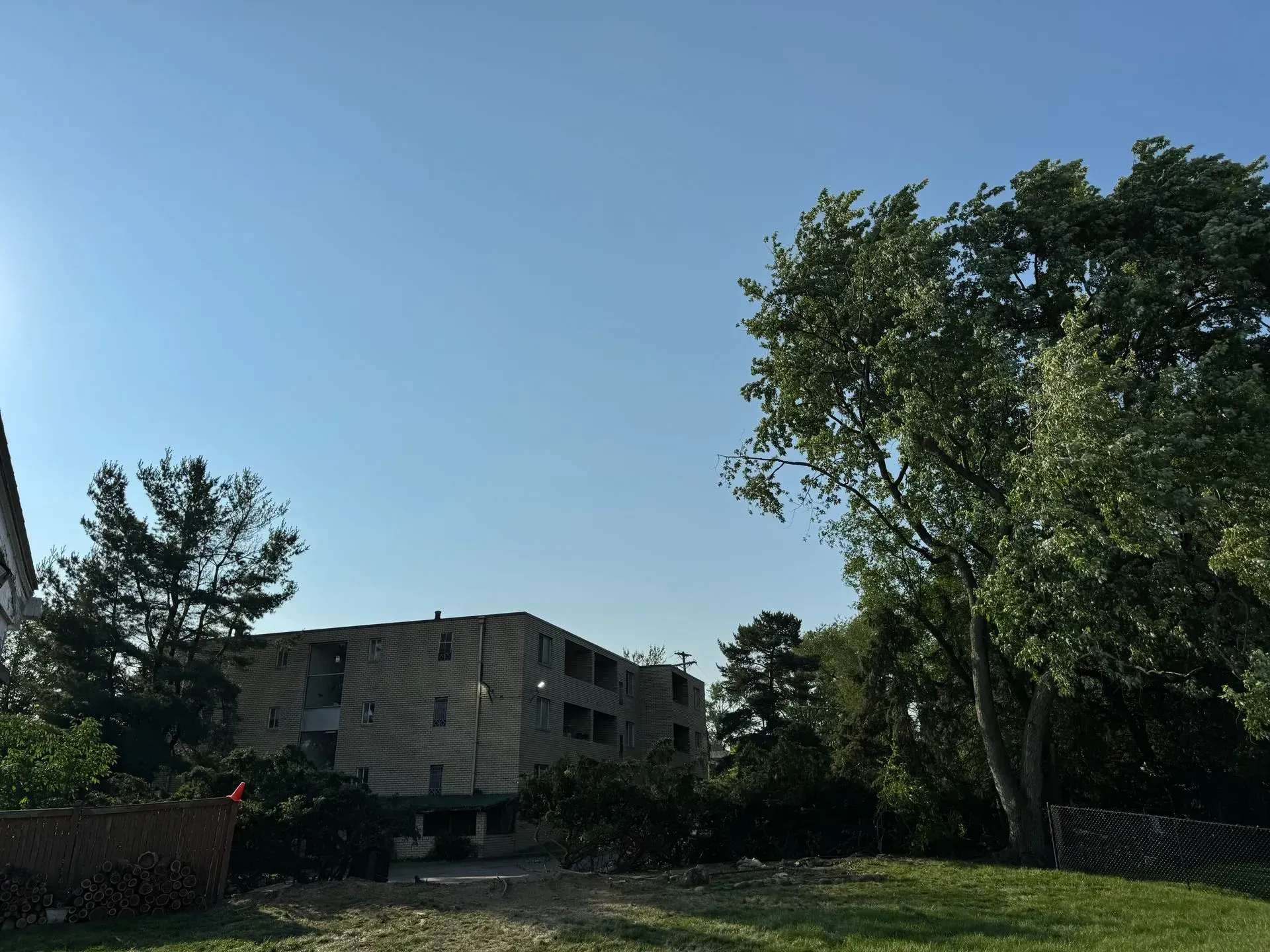 Apartment building on a sunny day, visible from a grassy area with trees and a clear blue sky.