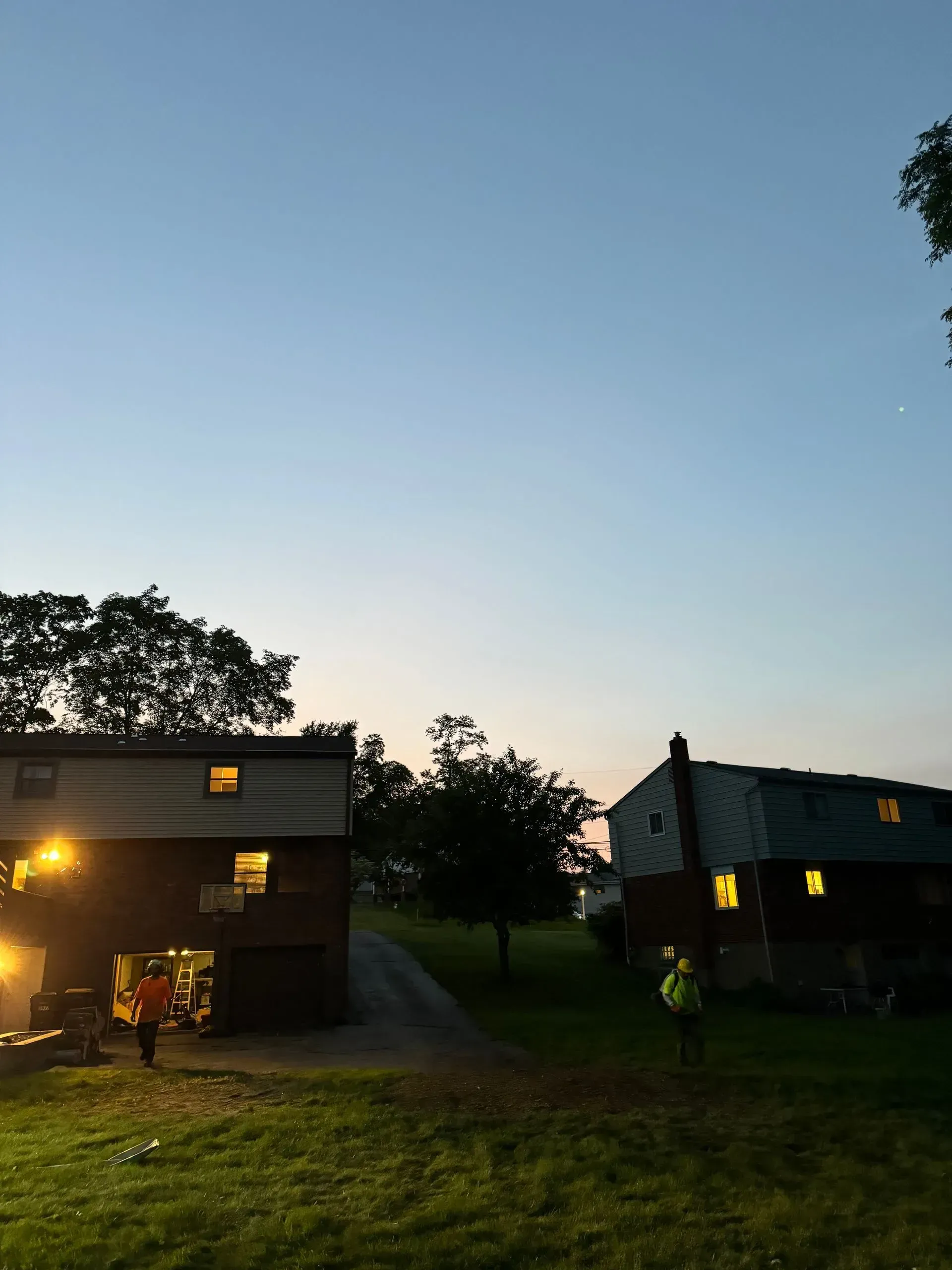Twilight scene with two houses, figures in yard, and a clear sky.