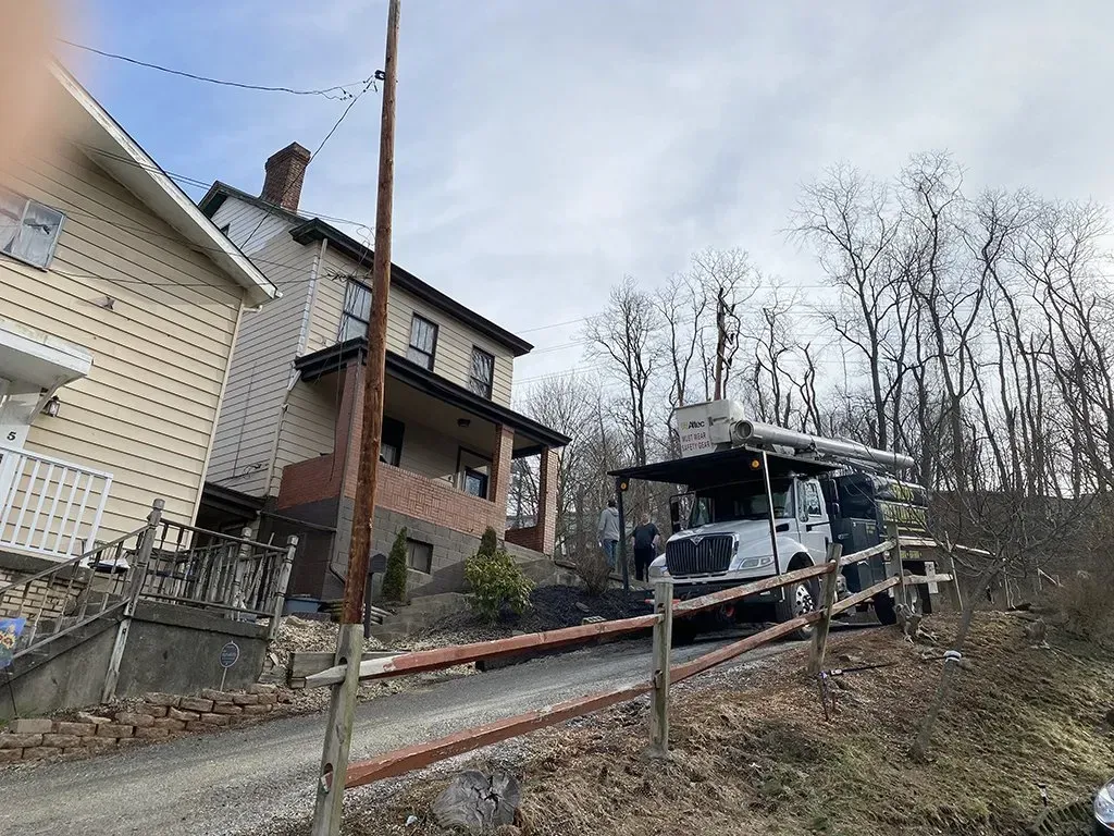 Jeep parked on a gravel driveway next to a two-story house with a brick porch and a wooden fence.