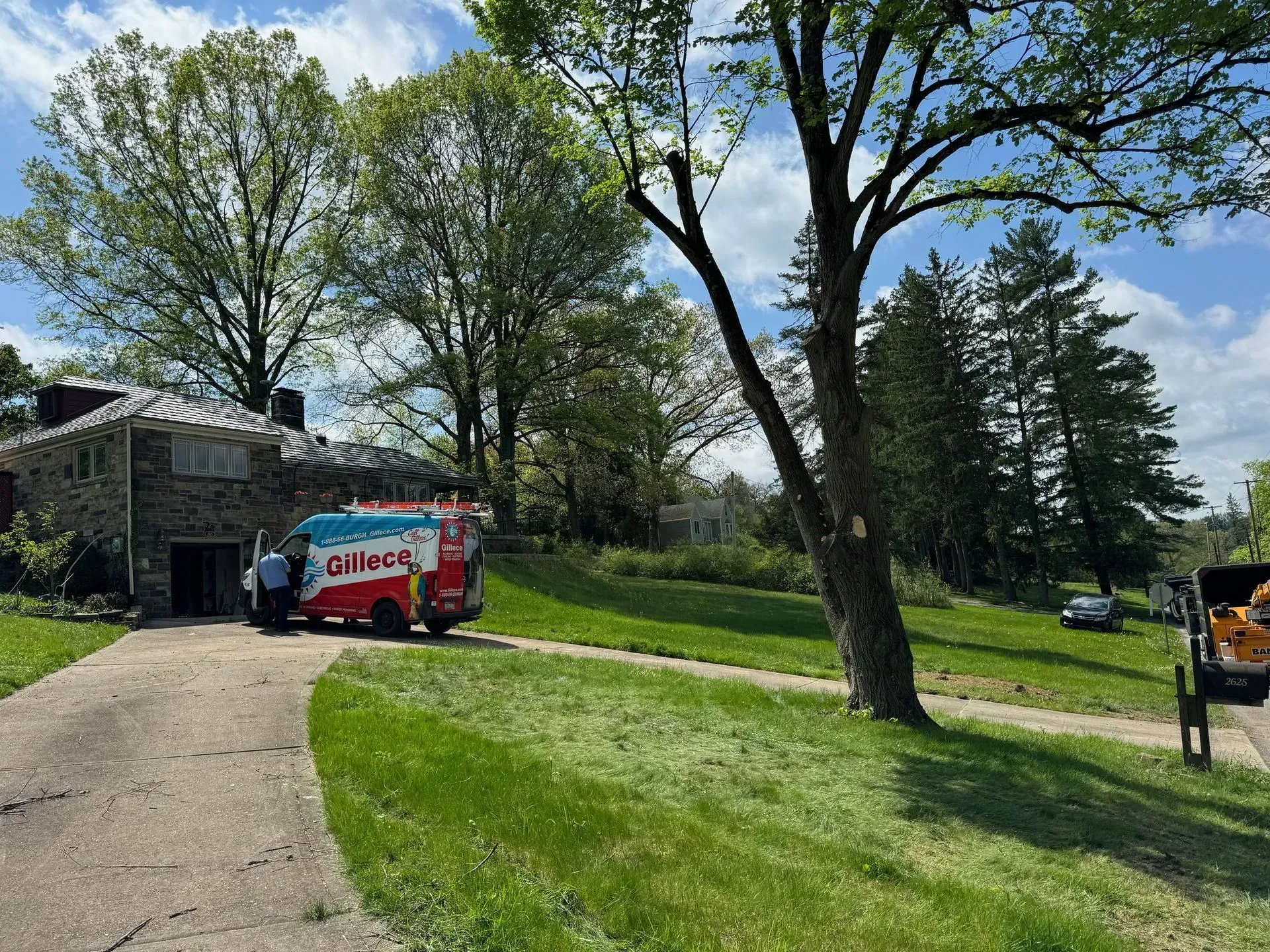 A service van parked in front of a stone house. A person stands near the van. Green lawn and trees.
