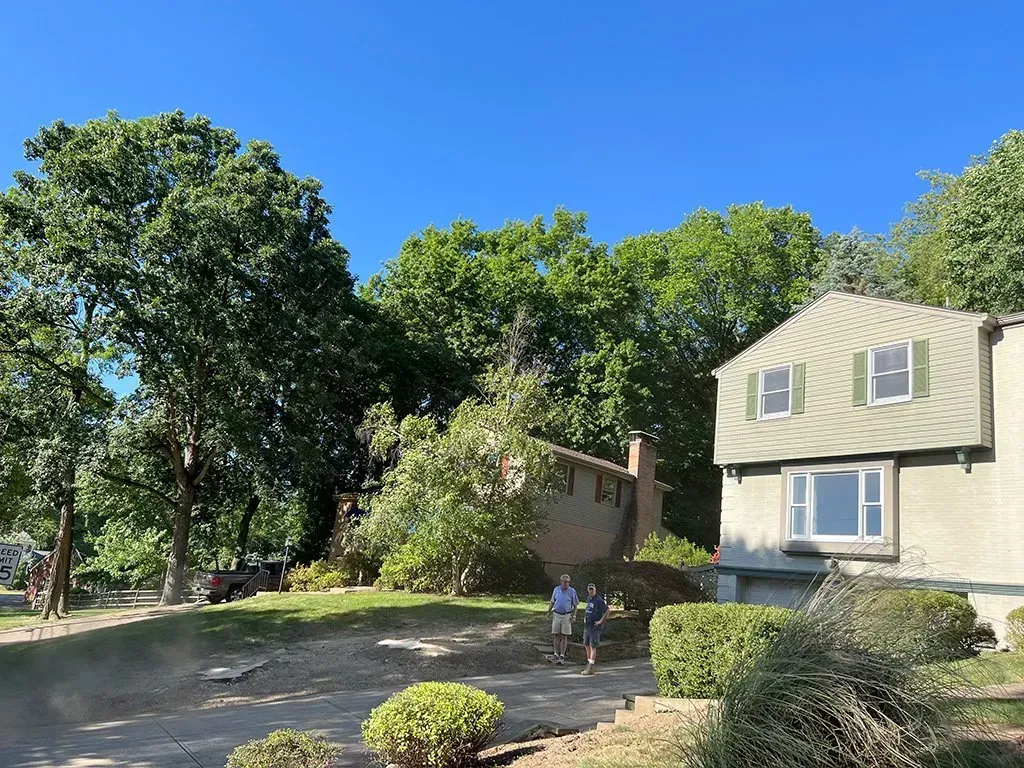 House next to trees with two people walking on a dirt path on a sunny day.