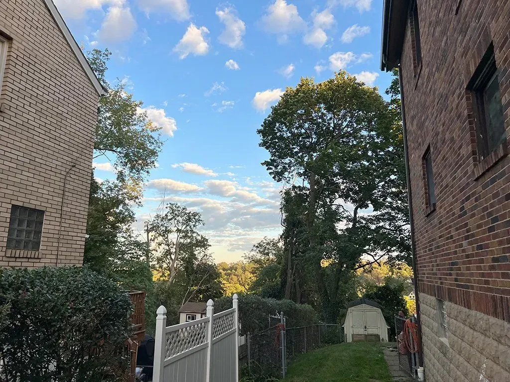 Brick buildings frame a view of trees, a white fence, and a partly cloudy sky.