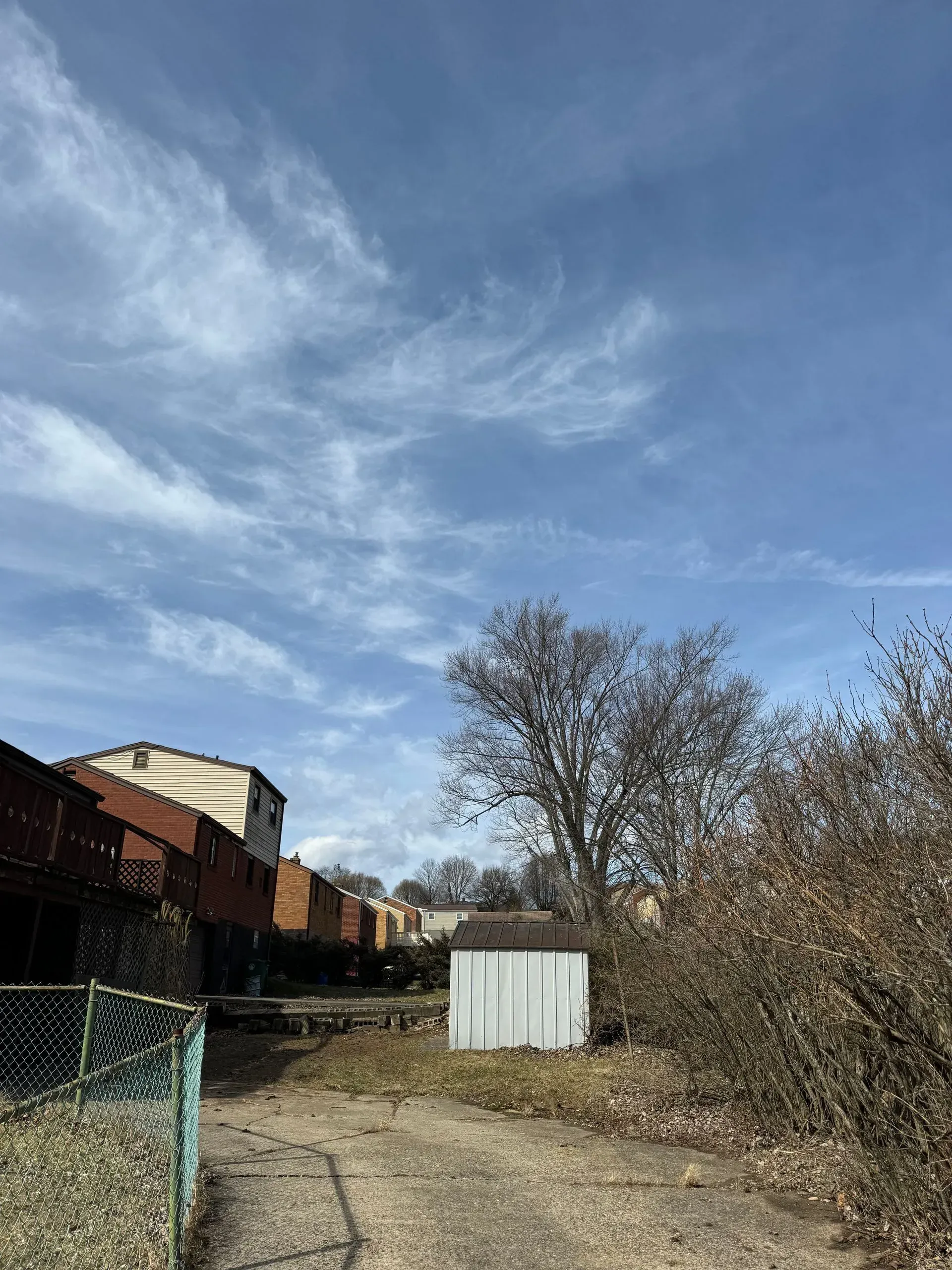 A partly cloudy sky above a driveway leading toward a small, white shed.