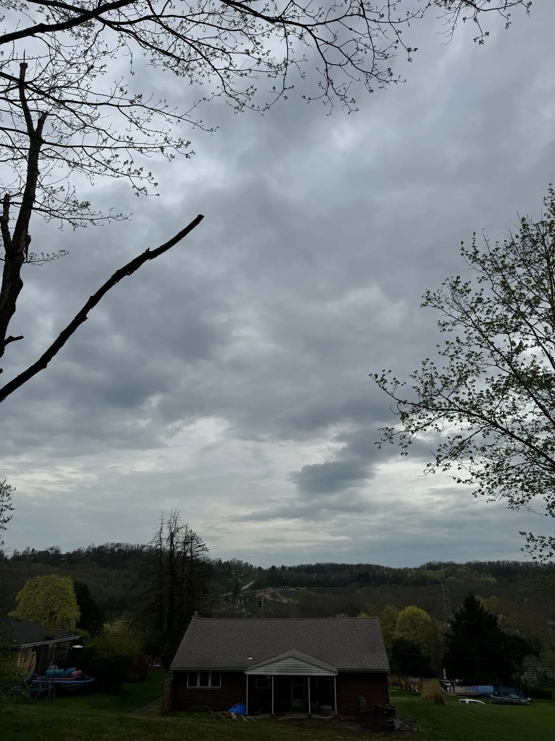 Overcast sky above a small, brown house, with trees in the foreground and rolling hills in the distance.