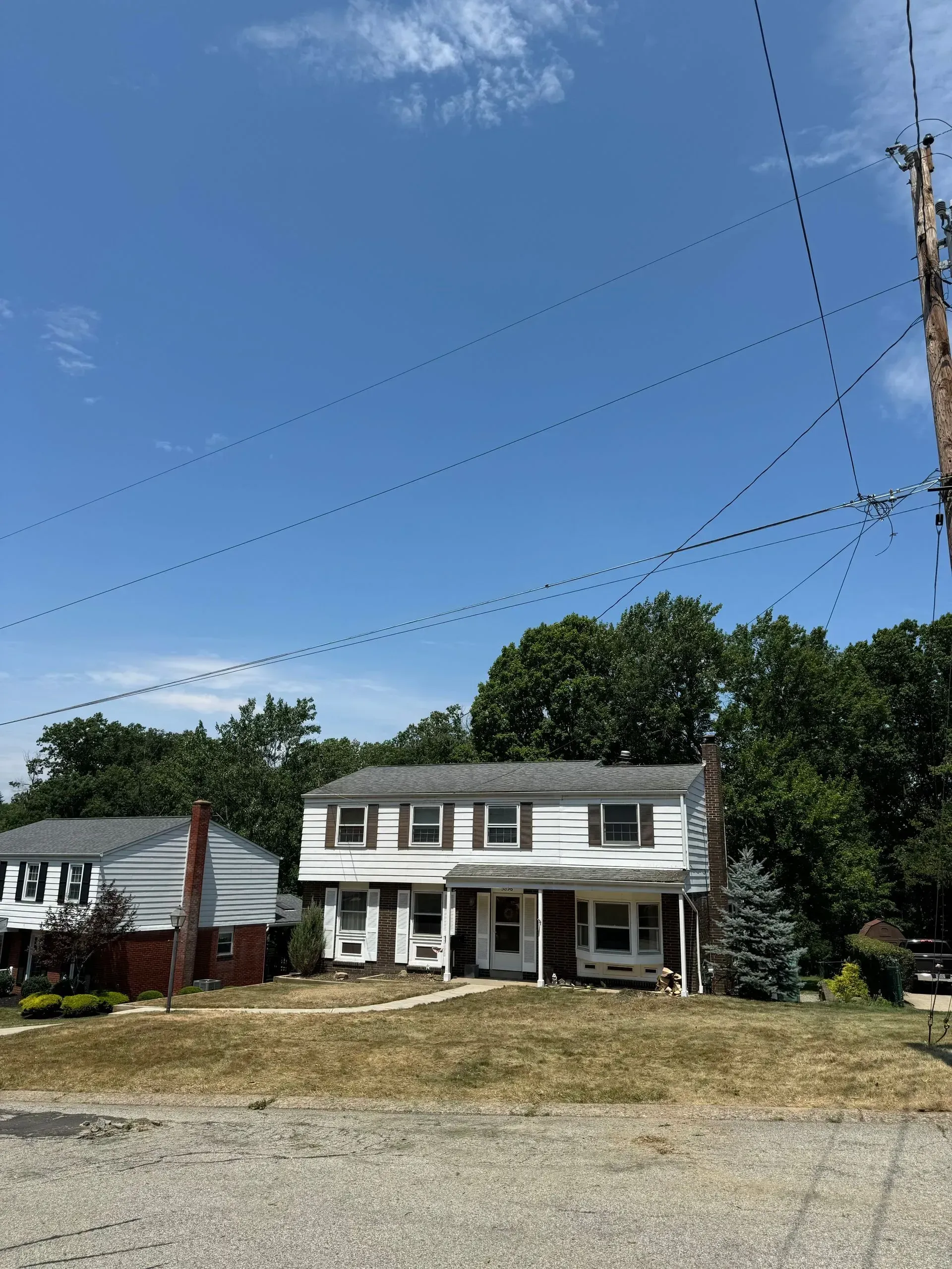 Two-story white house with brown trim, dry grass yard, blue sky. Power lines overhead.