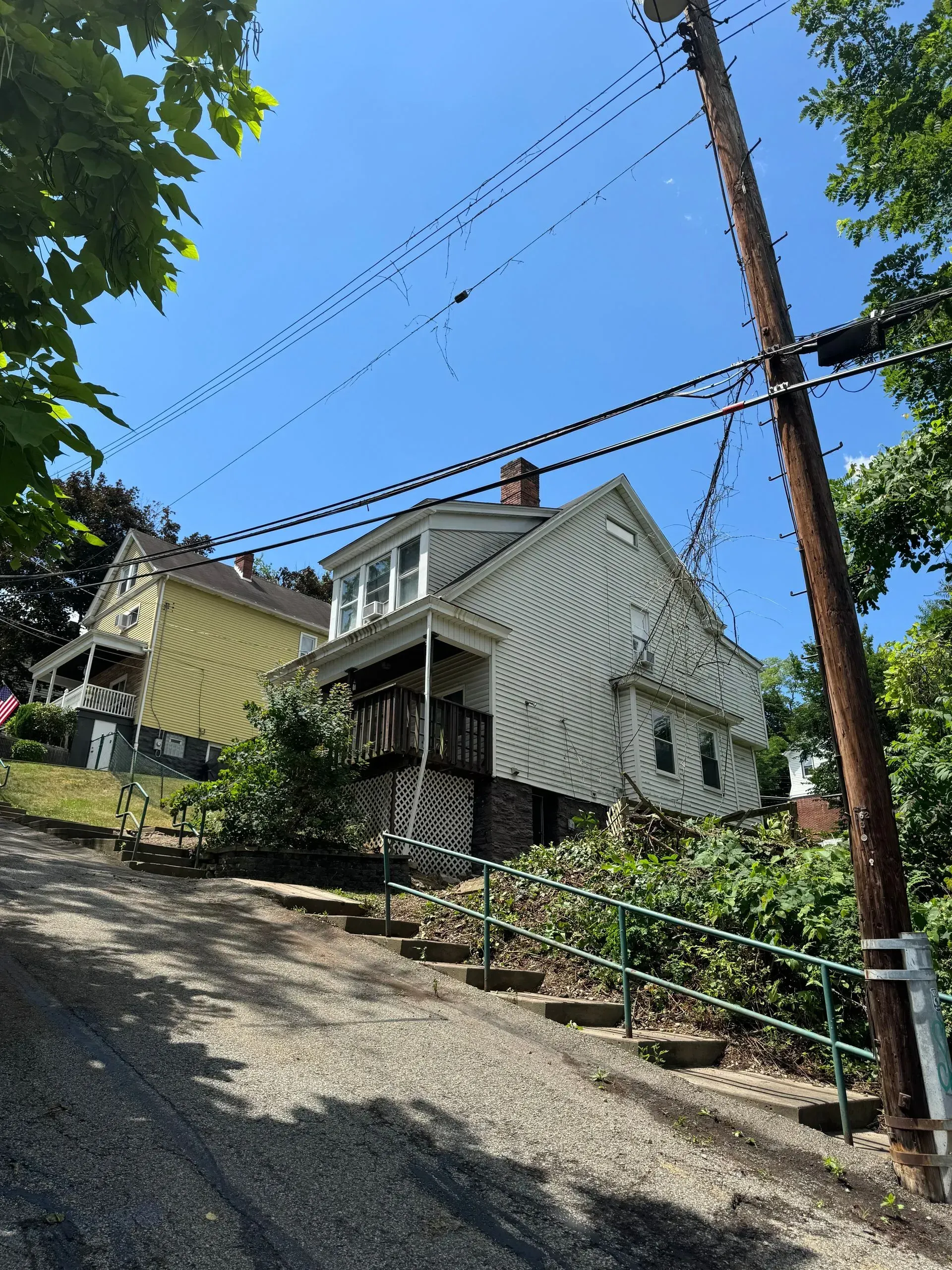 House on a hill with steps and a railing. White and yellow houses under a blue sky.