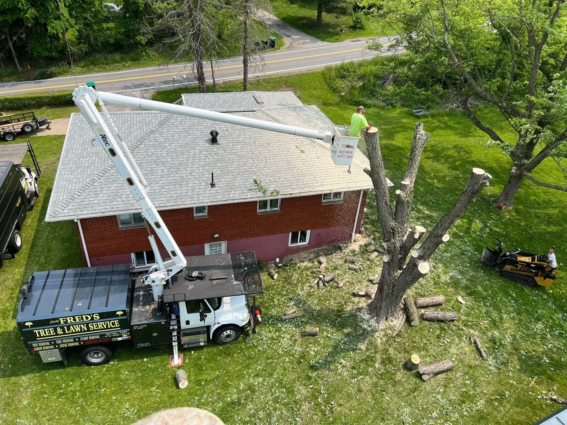 Four utility trucks with raised booms trimming trees near power lines.