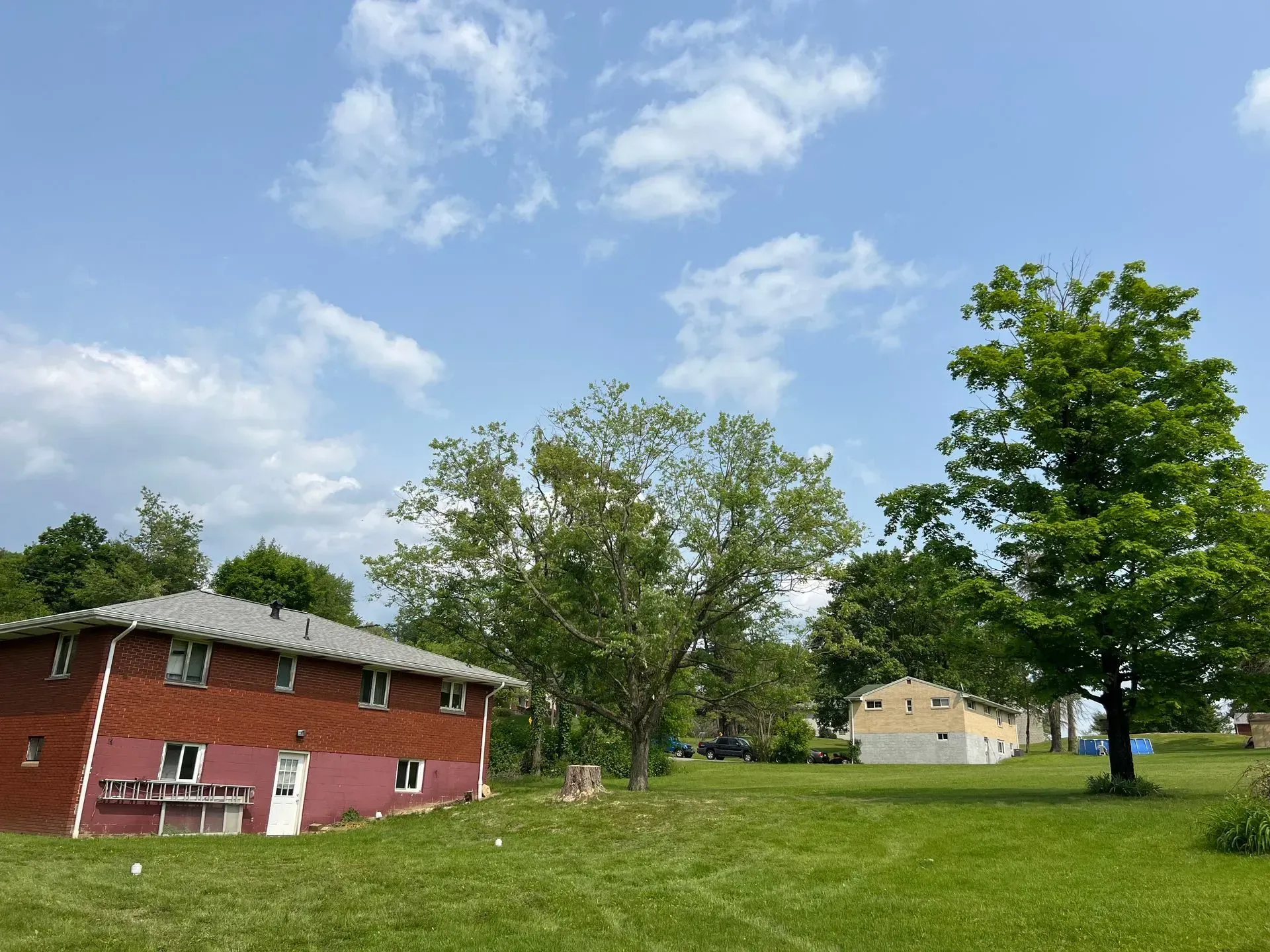 Lawn in front of red brick building and other homes under a cloudy blue sky, with trees.