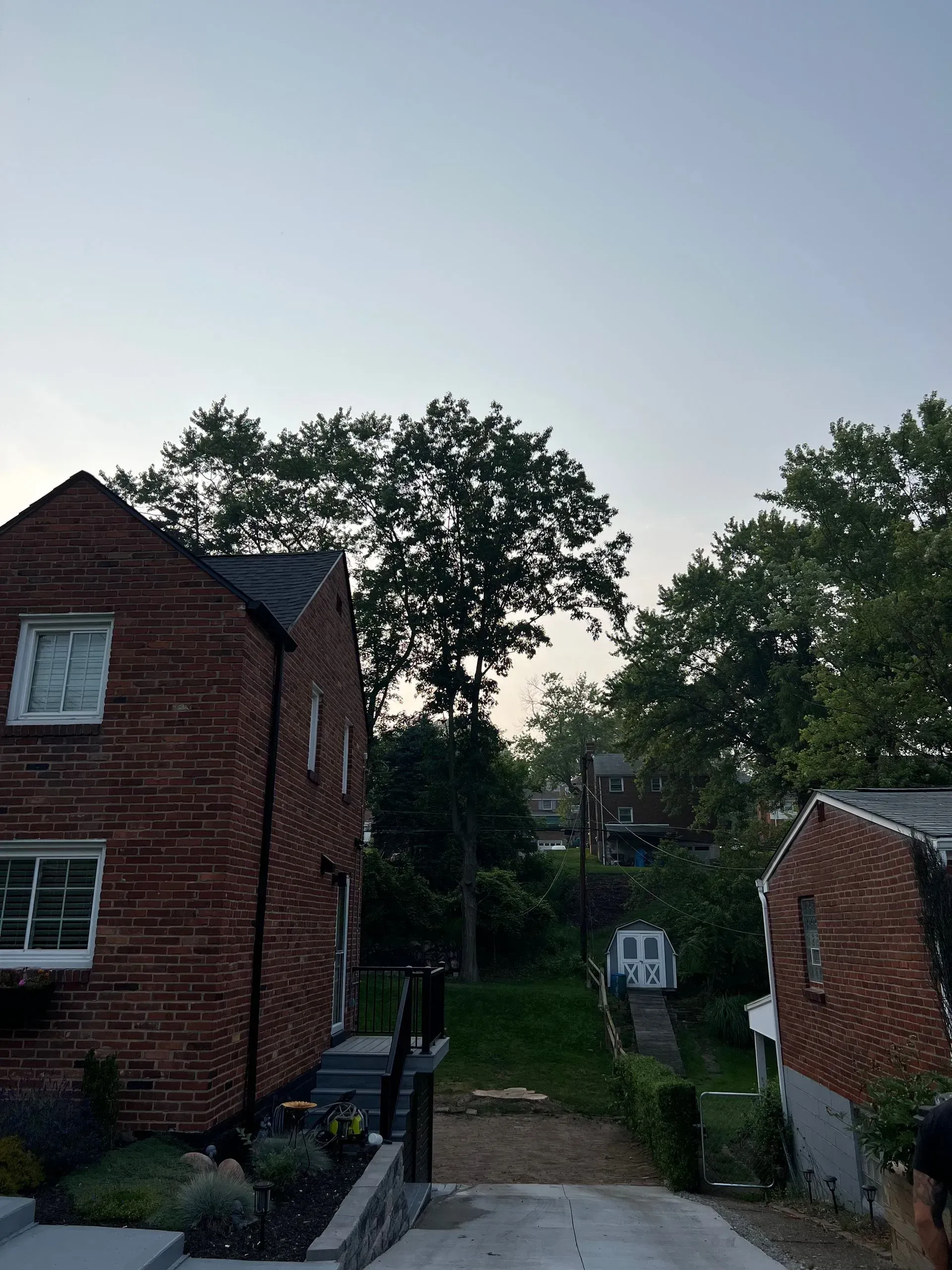 Brick houses flank a driveway leading uphill towards a tree-lined horizon under a dusky sky.