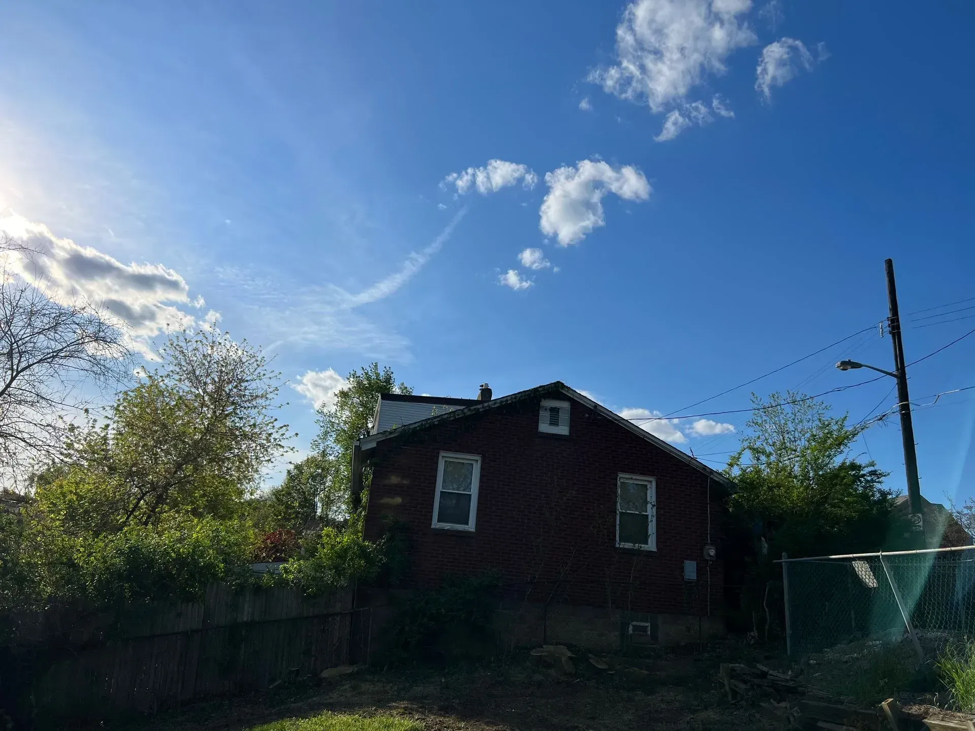 Red house with two windows under a blue sky with clouds and sunlight.