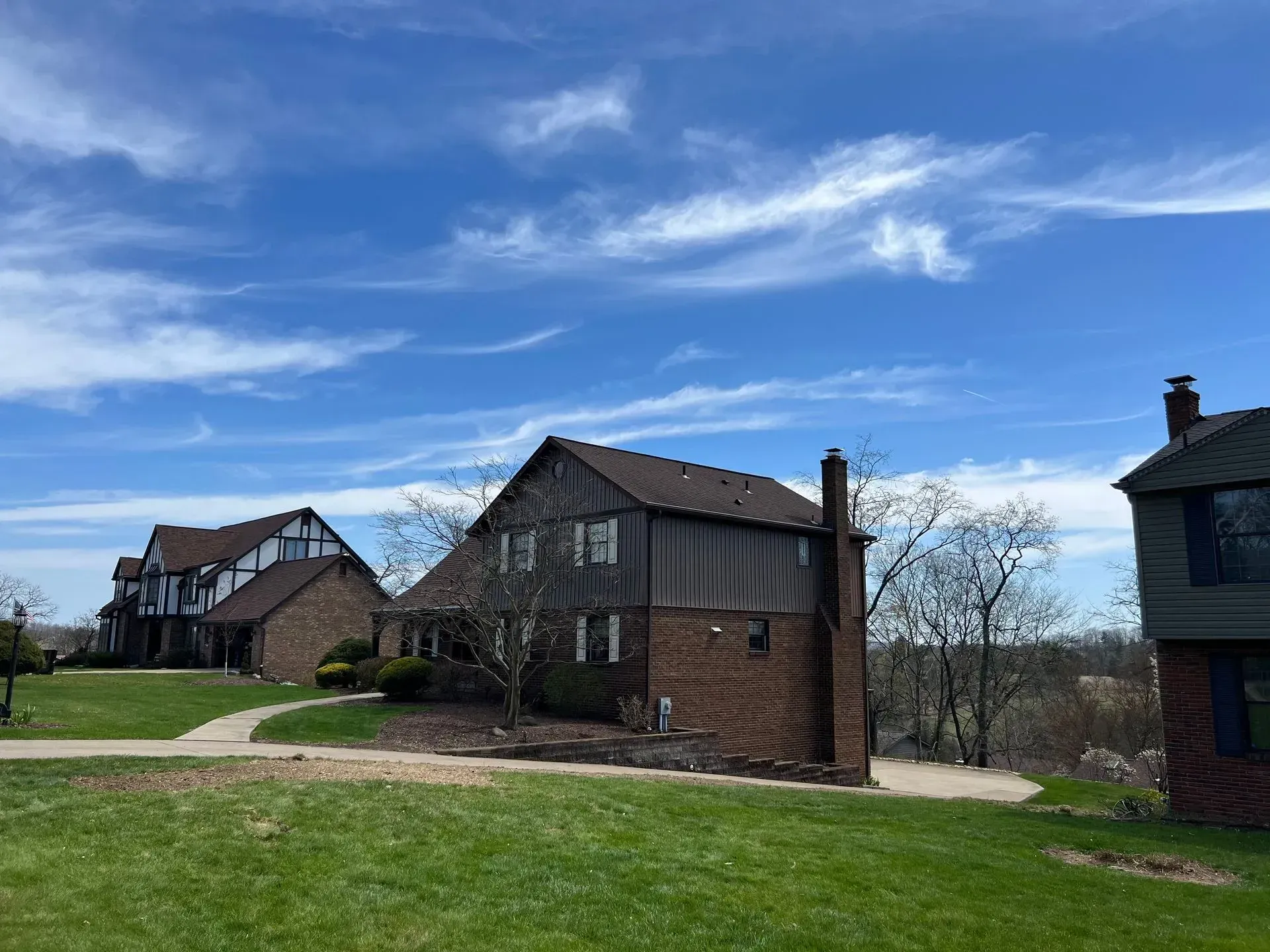 Houses with brick and dark siding under a blue sky with wispy clouds.
