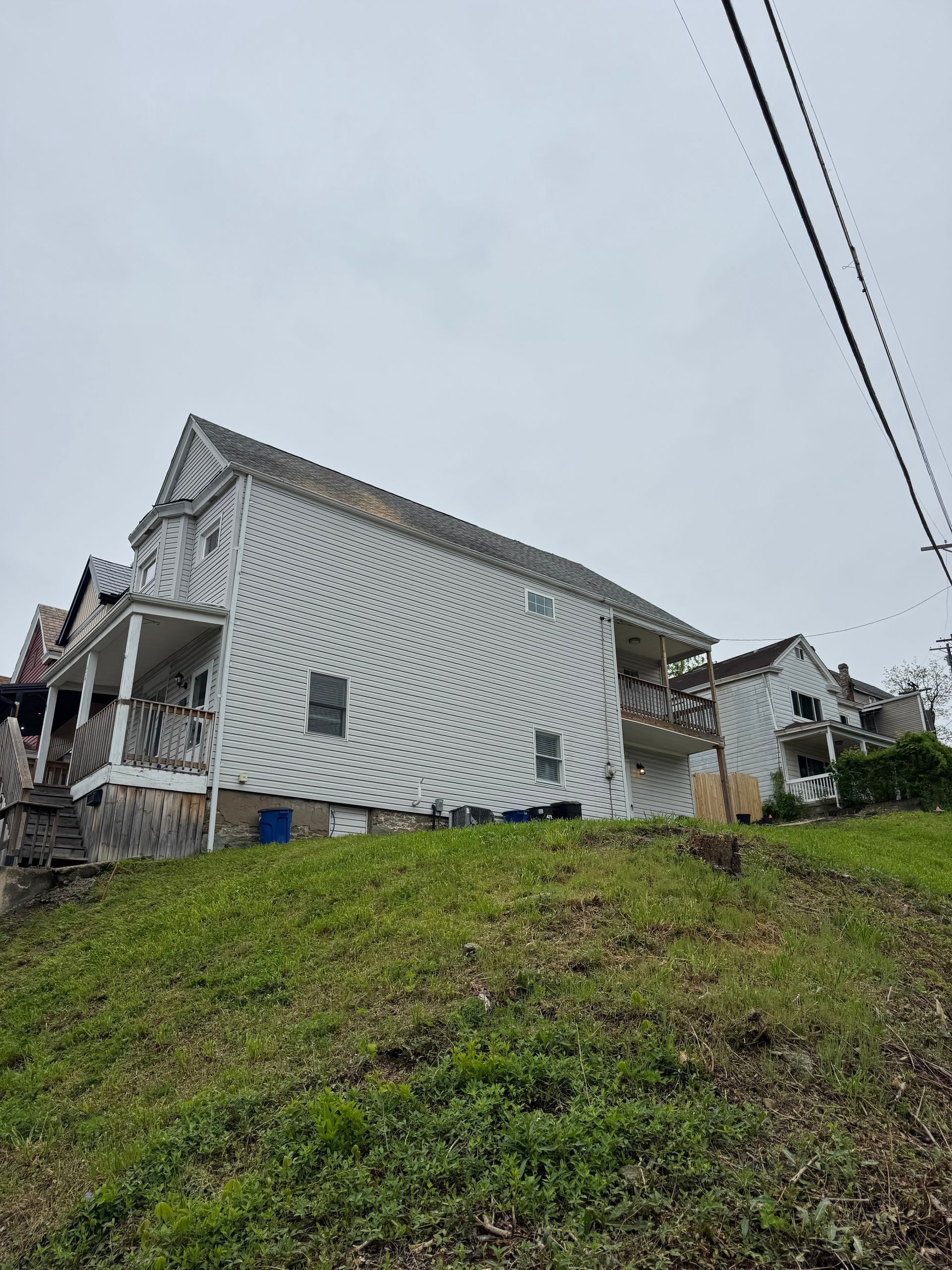 White house on a grassy hillside under cloudy sky with power lines overhead