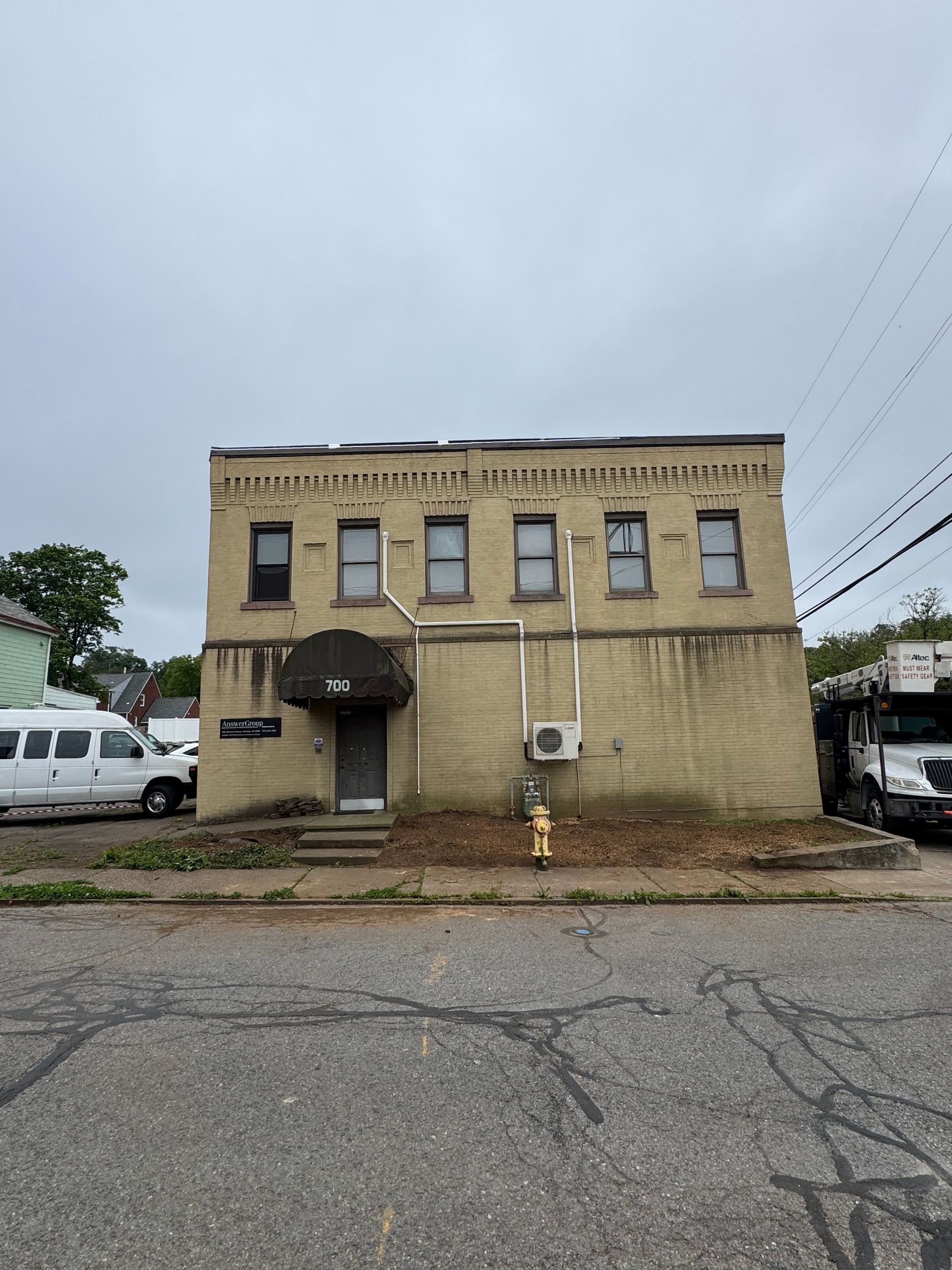 Two-story beige brick building with cracked pavement and cloudy sky, viewed from across an empty street