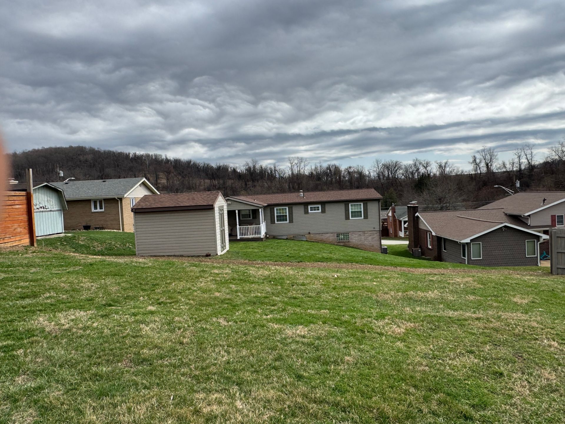 Grassy hill overlooking suburban houses under a cloudy sky