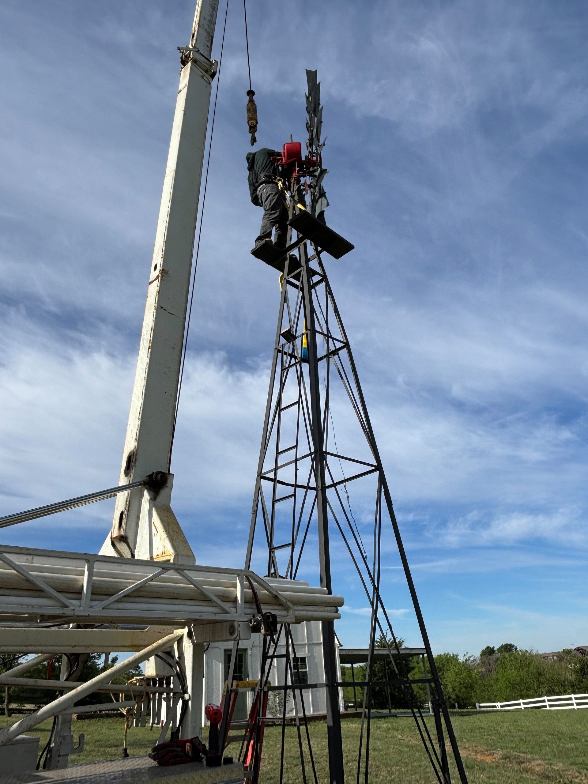 Workers on a tall lattice tower beside a crane, assembling equipment outdoors under a blue sky