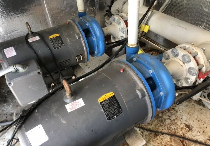 Two large black pumps with blue couplings and white pipes in an industrial room