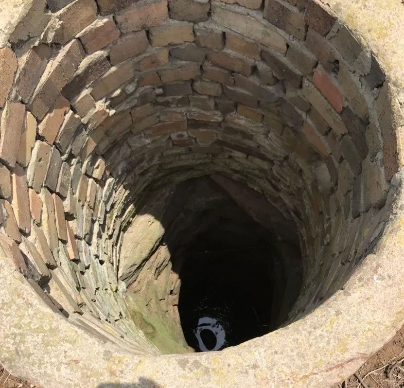Looking down inside a brick-lined well with dark water at the bottom