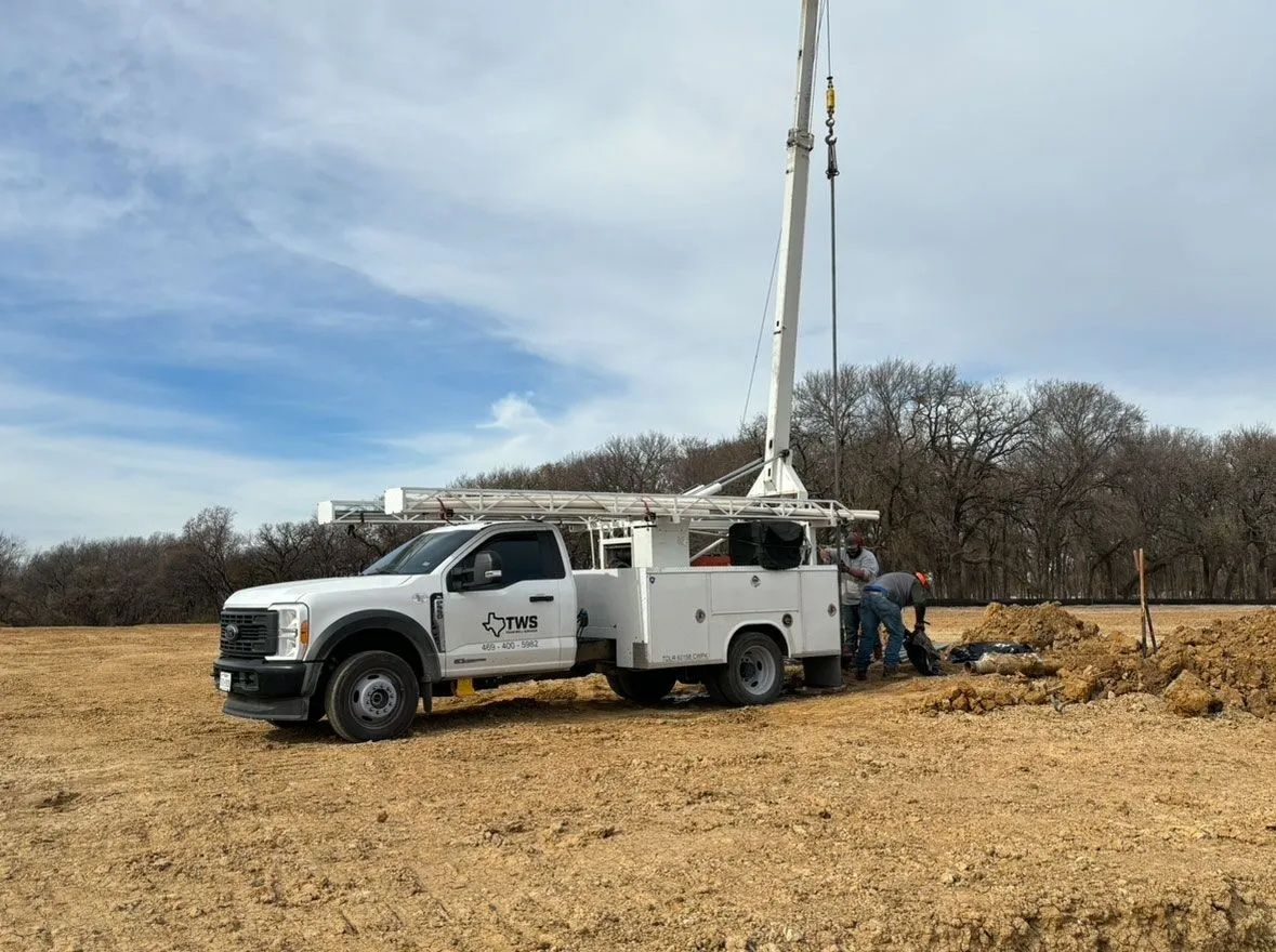 White utility truck with tall drill mast parked in a dry field under a cloudy sky