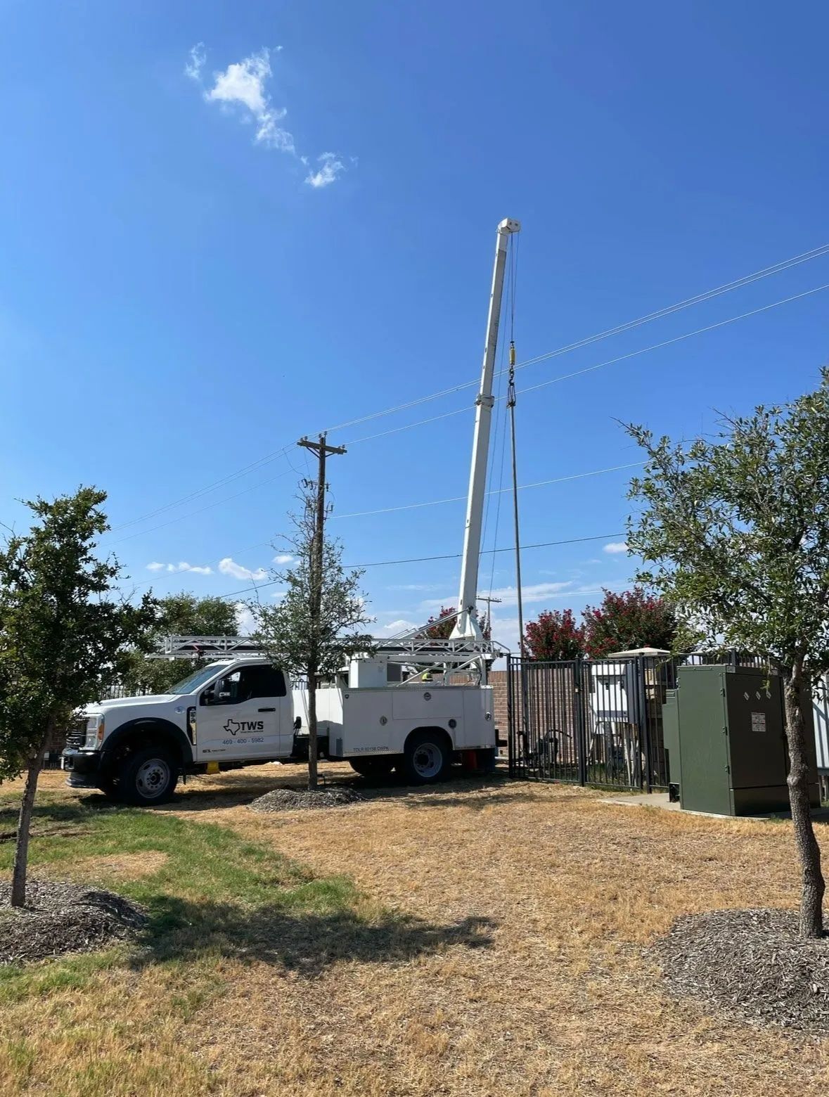 Utility truck with raised boom in a yard beside a fence under a clear blue sky.