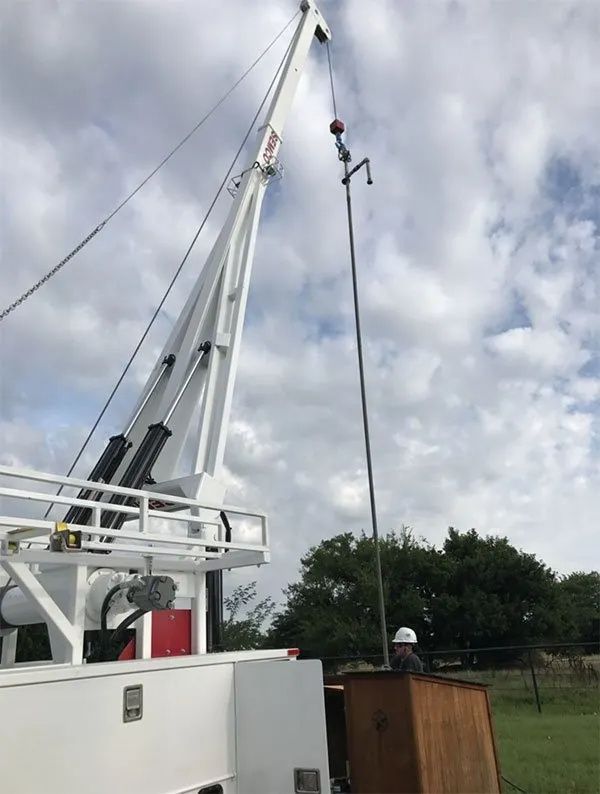 Crane lifting a cable on a cloudy outdoor work site, with a worker below and grassy field in background
