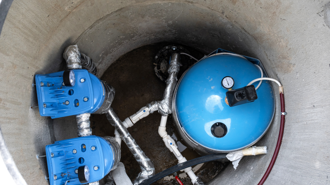 Blue industrial valves and piping inside a concrete pipe shaft.