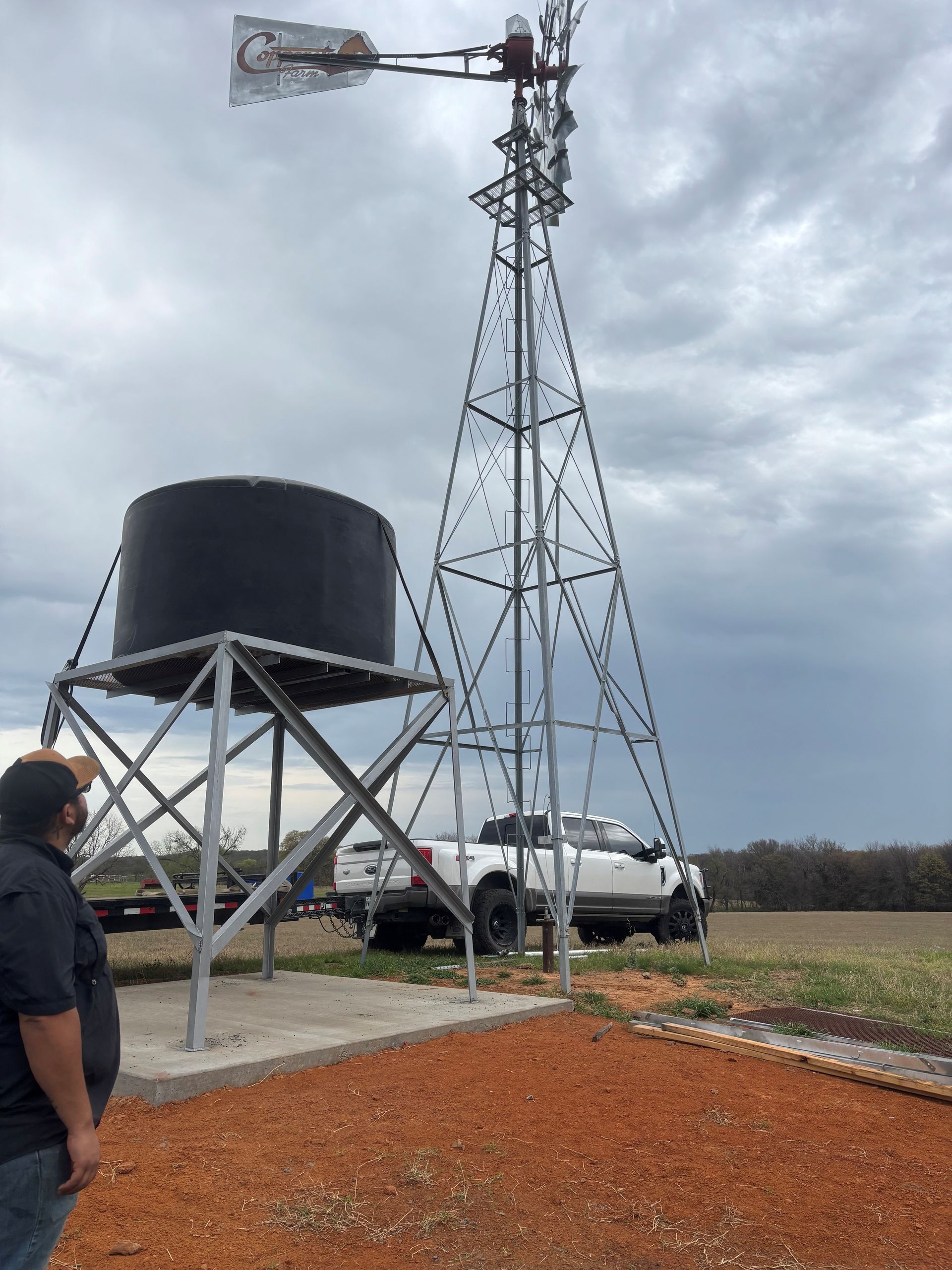 Weather station with tall anemometer tower beside a black water tank and parked truck under cloudy sky