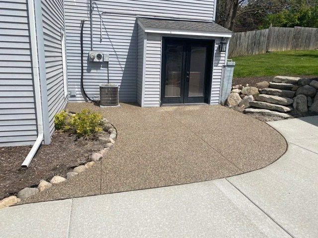 Backyard concrete patio curving to a small gray shed beside a house and rock retaining wall