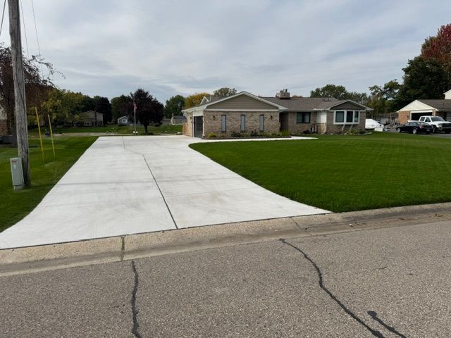 Suburban house with a wide concrete driveway and green lawn beside a quiet street
