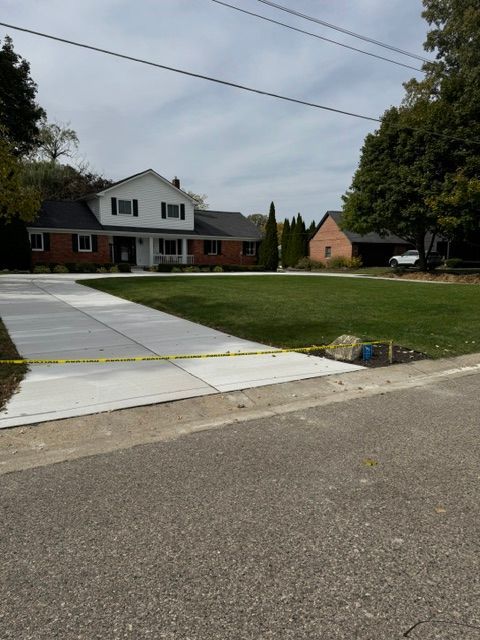 Suburban house with a long driveway, lawn, and overhead power lines under a cloudy sky